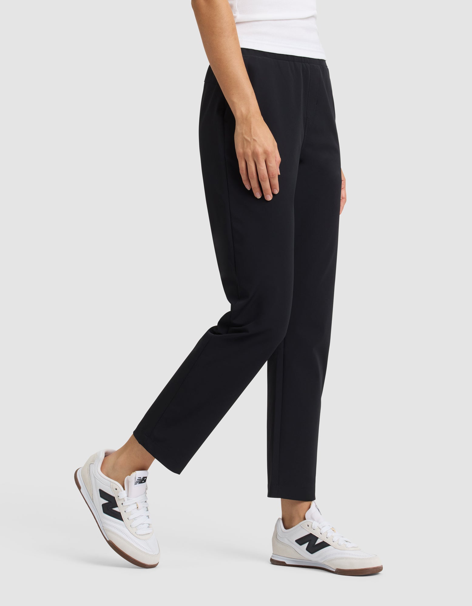 A person wearing Cozy Earth's Women's Always Cropped Pant in black, a white top, and white sneakers stands against a plain light gray background. Only the lower torso and legs are visible. |Color:Jet Black