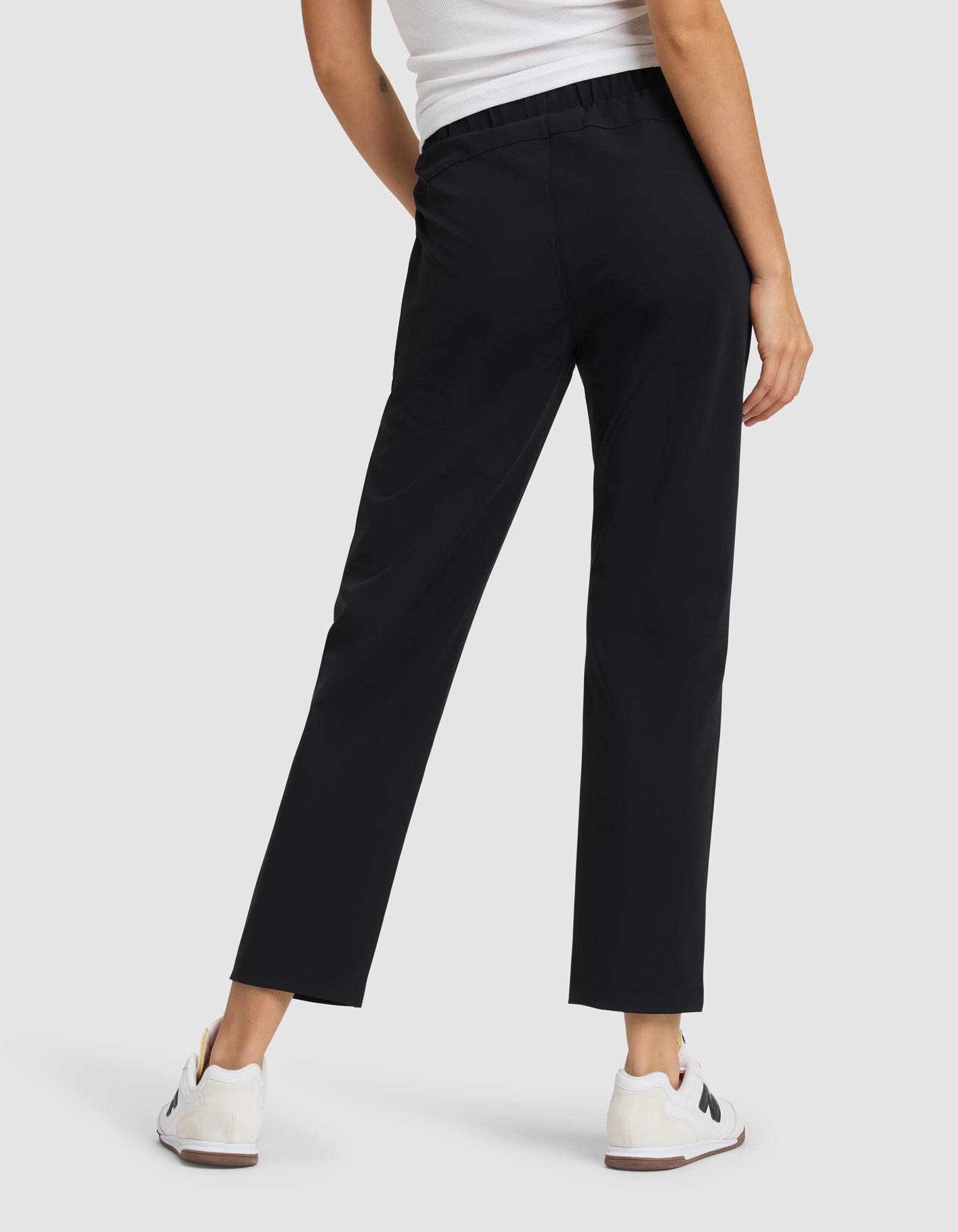 A person in Cozy Earth's Women's Always Cropped Pant, paired with a white sleeveless top and white sneakers, stands facing away from the camera against a plain light background. |Color:Jet Black