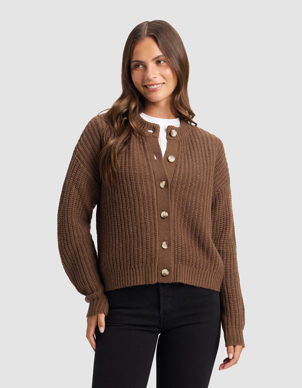 A woman with long brown hair stands smiling against a light gray background, wearing the Cozy Earth Women's Arden Cardigan over a white top and black pants.|Color:Cedar