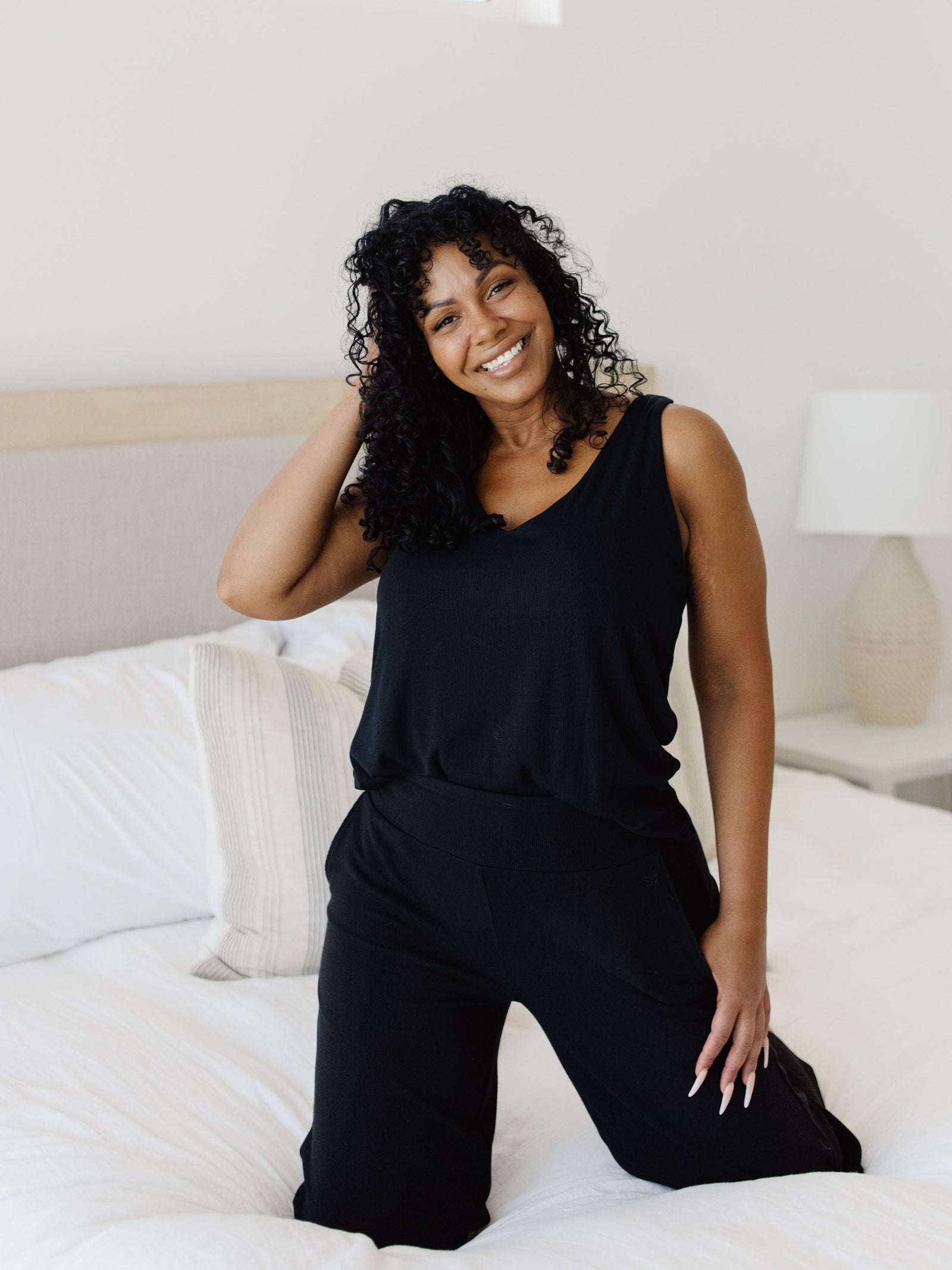 Woman wearing a black Cozy Earth Rib Knit Bamboo V-Neck Lounge Tank kneels on a bed