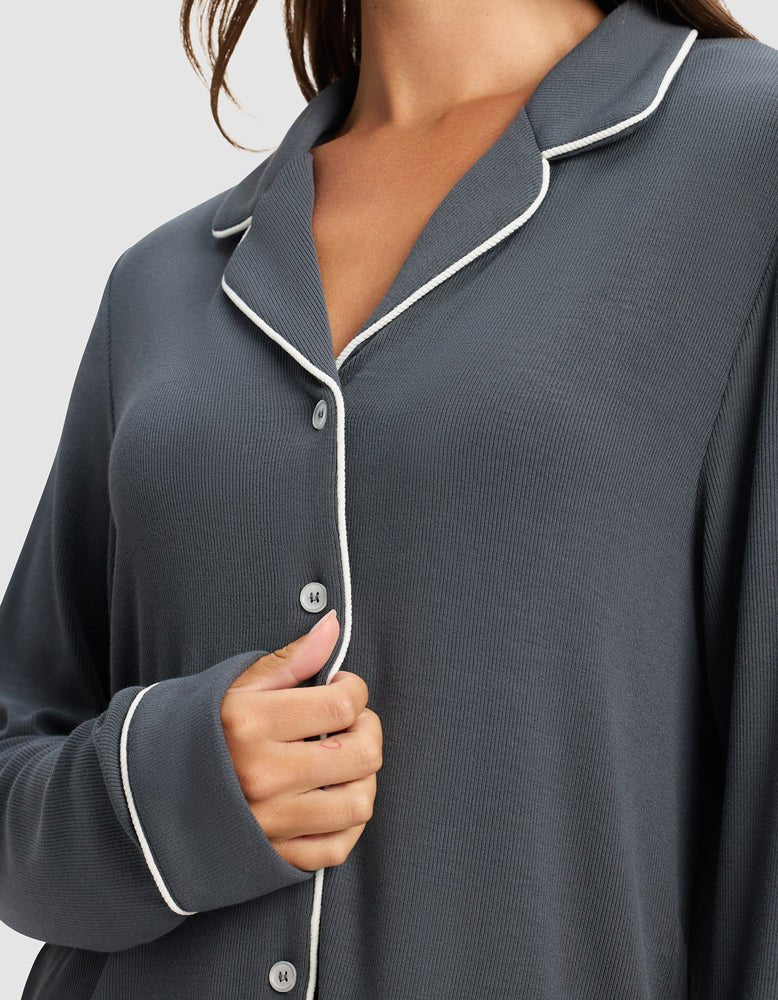 A woman wears the Cozy Earth Women's Bamboo Rib-Knit Classic Long Sleeve Pajama Top in dark gray with white piping, holding the front of the button-up shirt with her left hand.
