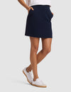 A person wears the Cozy Earth Women's Brushed Bamboo Skirt in navy, styled with a white t-shirt and gum-soled white sneakers, standing against a plain light gray background. |Color:Navy