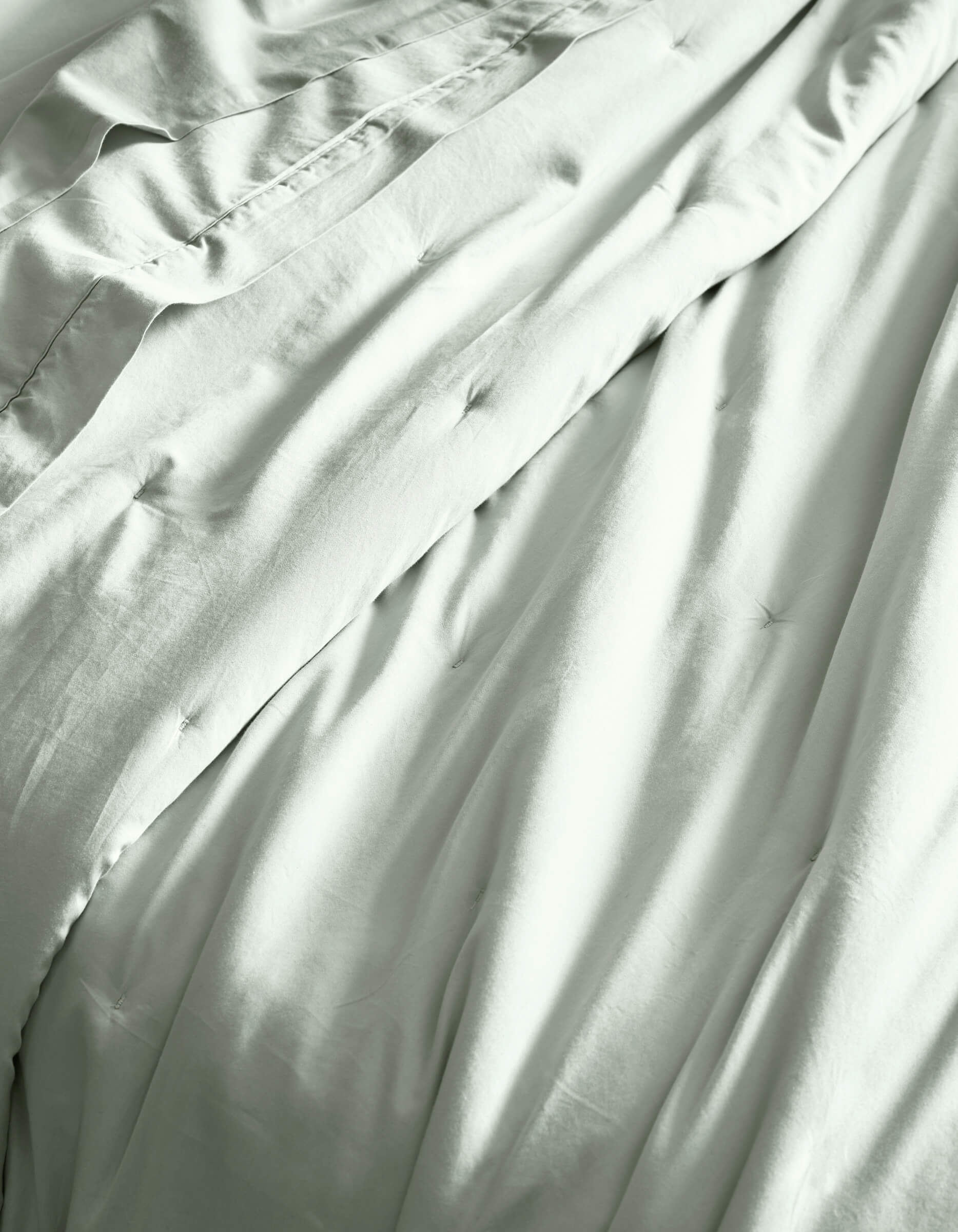 Close-up of Cozy Earth’s Soft-Wash Cotton Quilt, showcasing its light color, gentle folds, and subtle tufted details for a soft, comfortable, and inviting bed.|Color:Laurel
