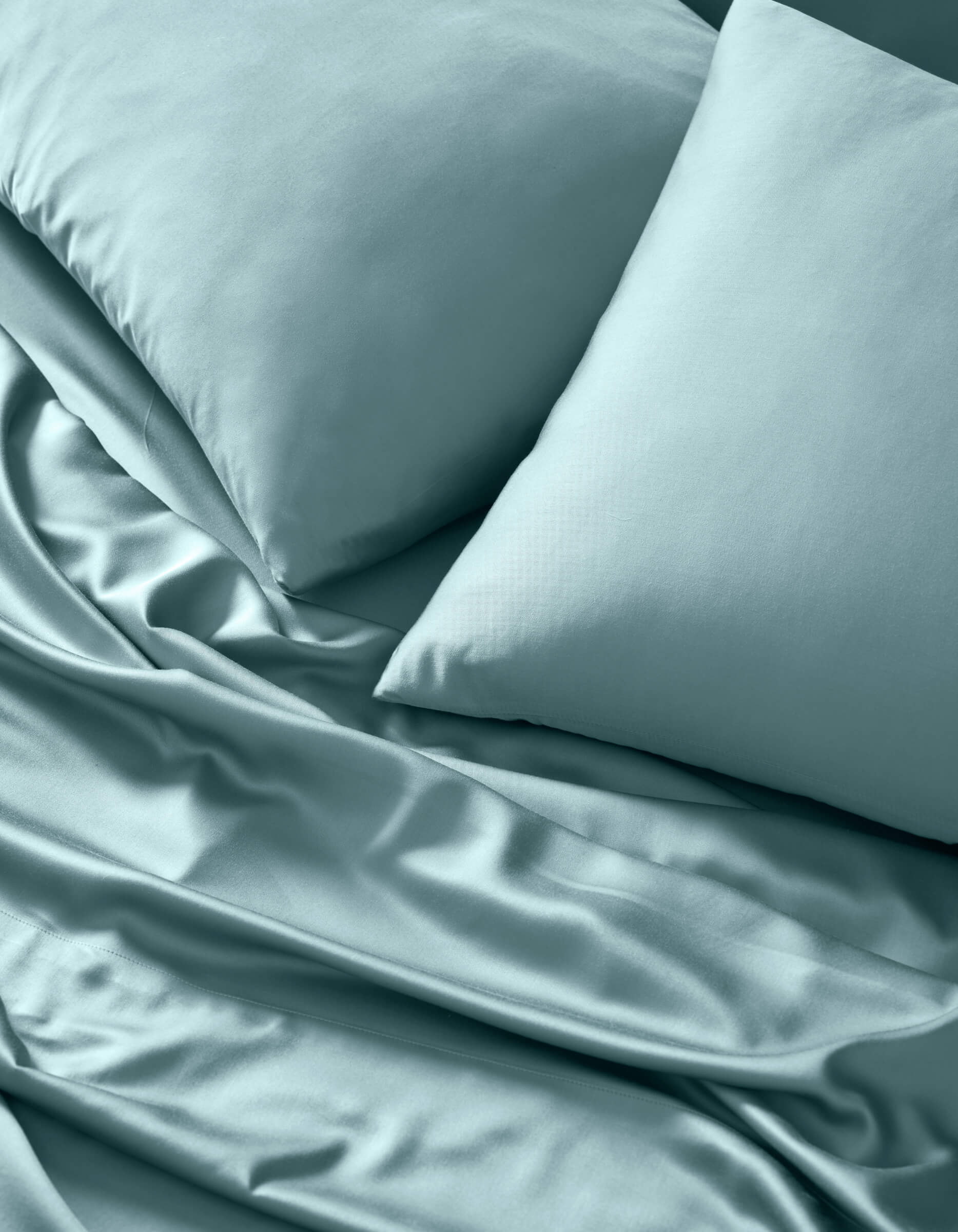 A close-up of Cozy Earth's Bamboo Sheet Set in light blue, neatly arranged with two matching pillows. The smooth, soft fabric shows subtle folds and a gentle sheen for an inviting look.|Color:River