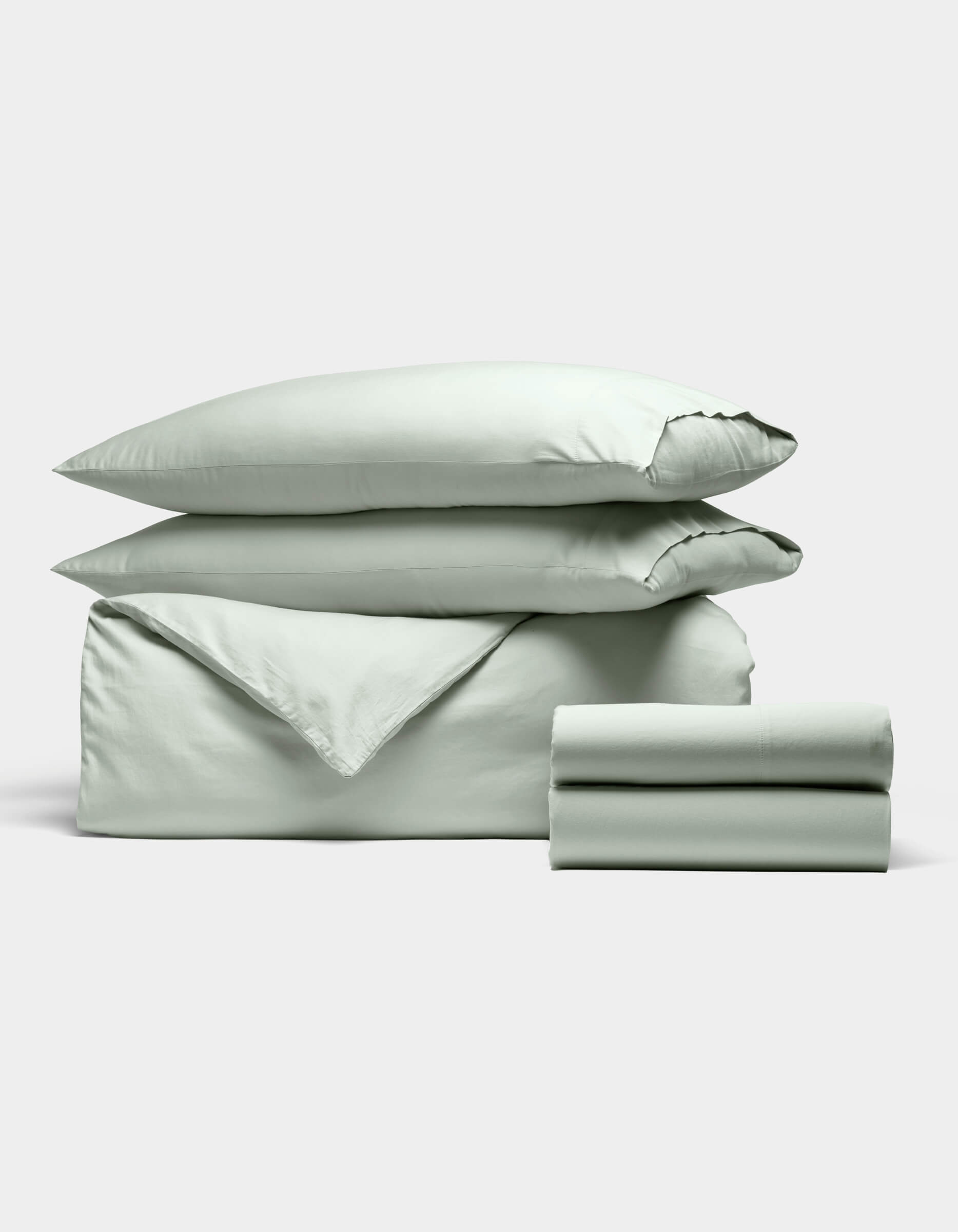 The Cozy Earth Soft-Wash Cotton Bedding Deluxe Bundle, shown neatly folded against a white background, includes two pillows, a duvet cover, and two sheets in light green.|Color:Laurel