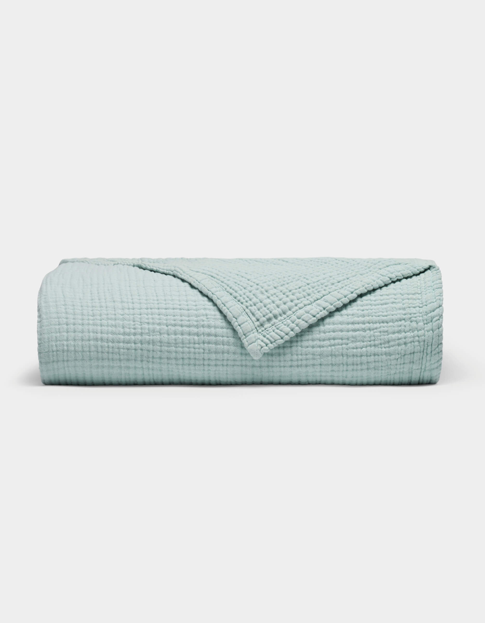 The Cozy Earth Cotton Gauze Blanket is neatly folded in light blue with a textured, grid-like pattern on a plain white background. One corner is turned down to reveal the inner side.|Color:Tide