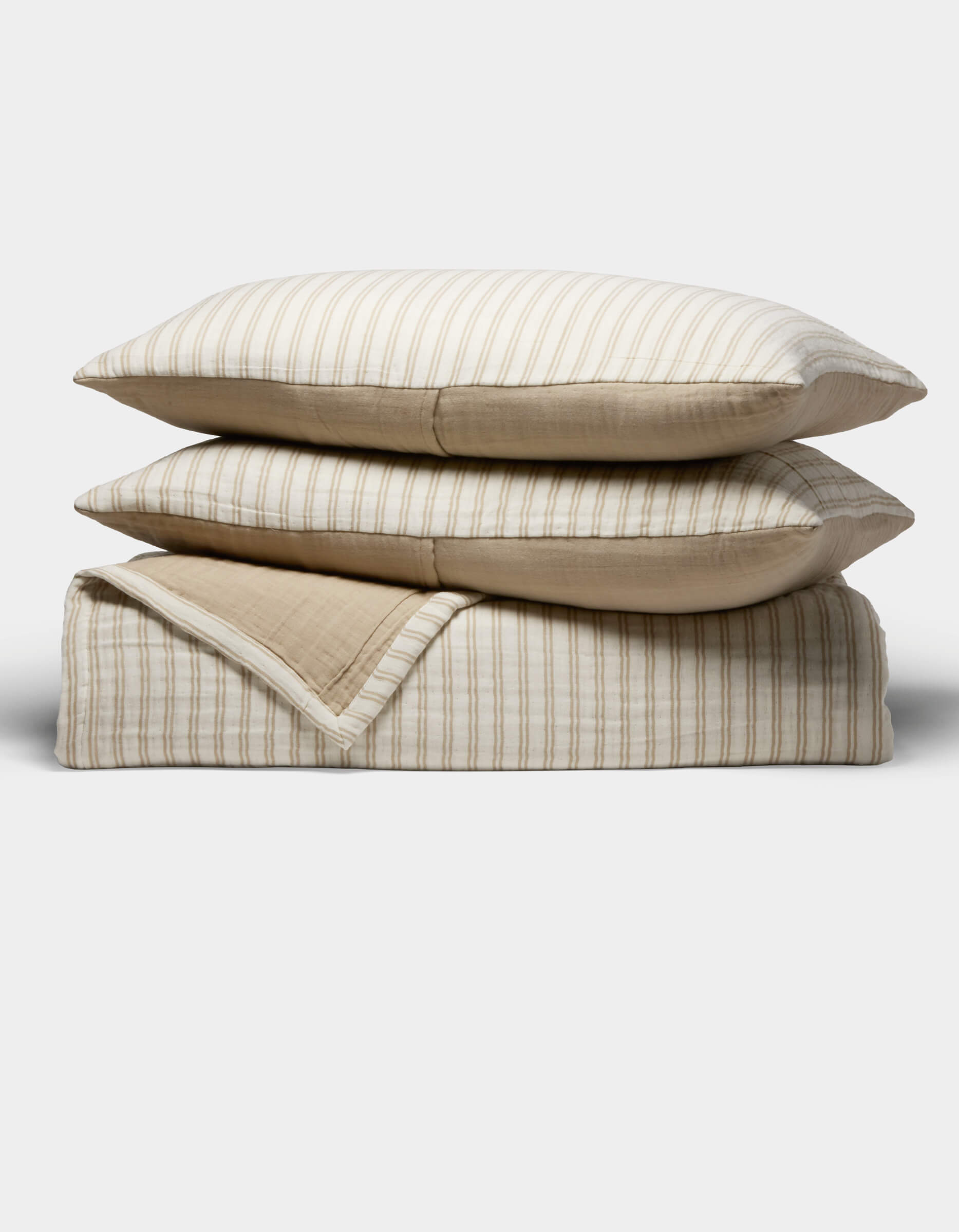 The Cozy Earth Waterfront Coverlet Bundle features two beige and white striped pillows stacked on a matching folded quilt, all set against a plain white background.|Color:Sandalwood Stripe
