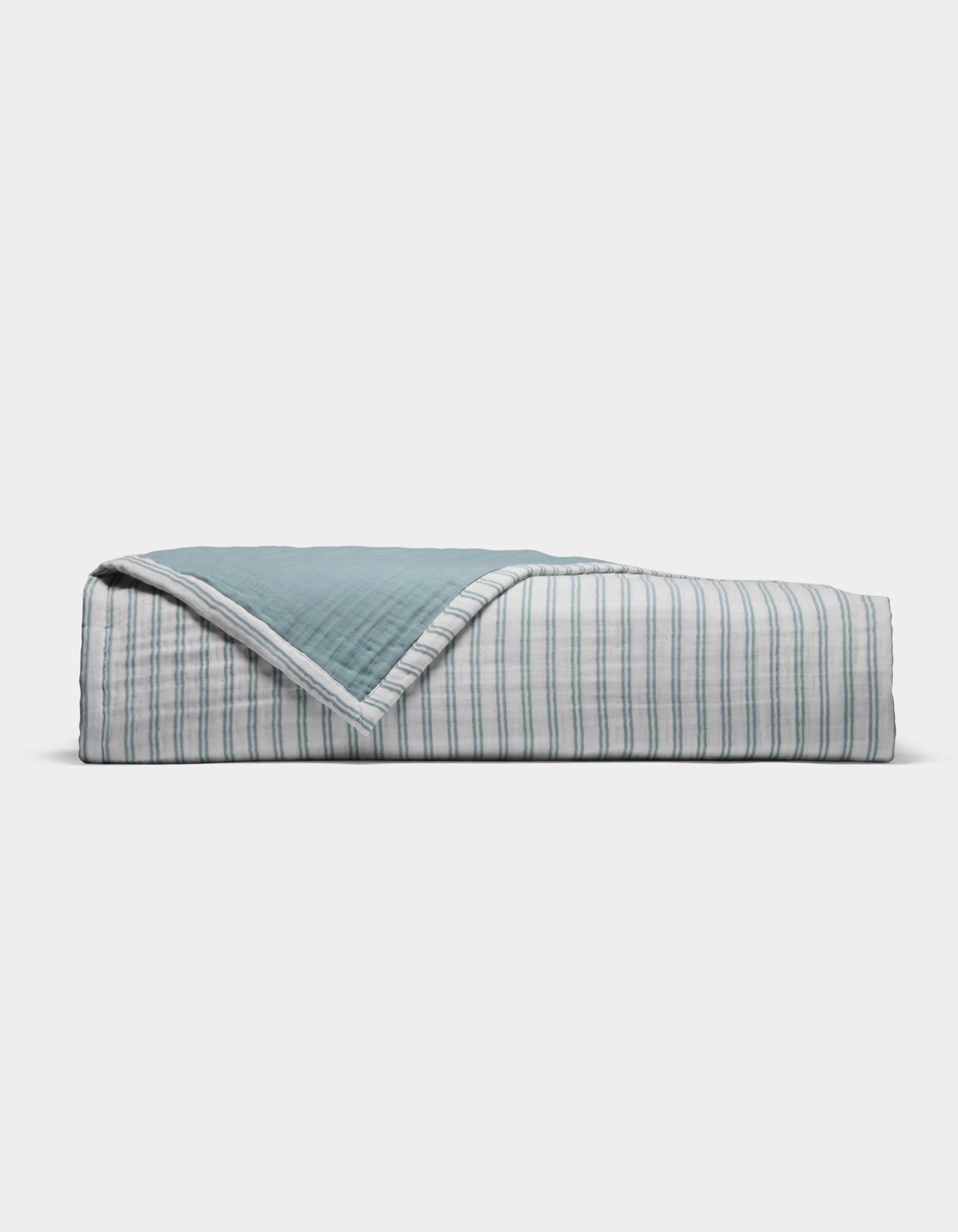 The Cozy Earth Waterfront Coverlet is a neatly folded quilt with a blue top and a white underside featuring thin blue stripes, displayed against a plain white background.|Color:River Stripe