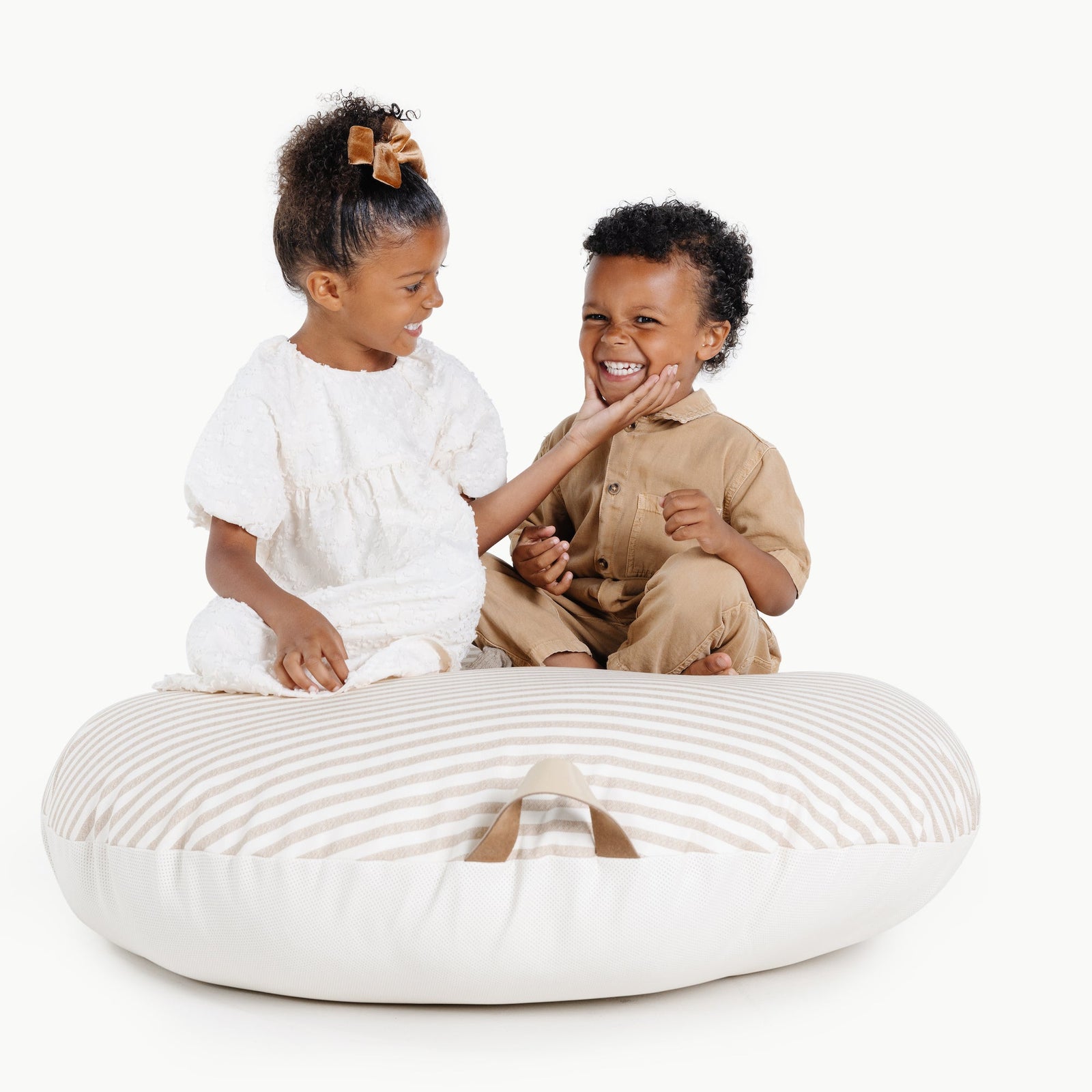 Two young children enjoy the Gathre Wholesale Floor Cushion. The girl in a white dress touches the smiling boy’s cheek as they play together, both appearing cheerful against a plain white background.