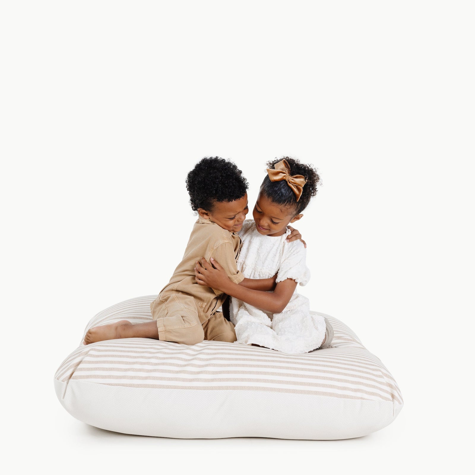 Two young children sit and hug on a Gathre Wholesale Floor Cushion, smiling at each other against a plain white background.