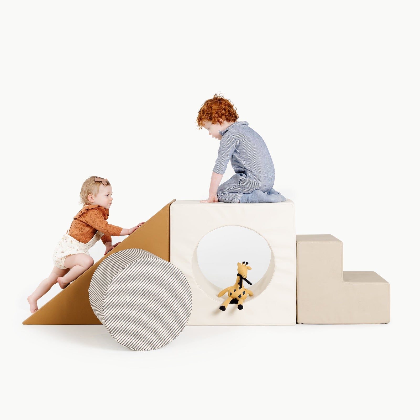 Two young children play on the Gathre Wholesale Block Playset, featuring a ramp, steps, and a block with a circular cutout holding a plush giraffe toy. The scene is set against a plain white background.