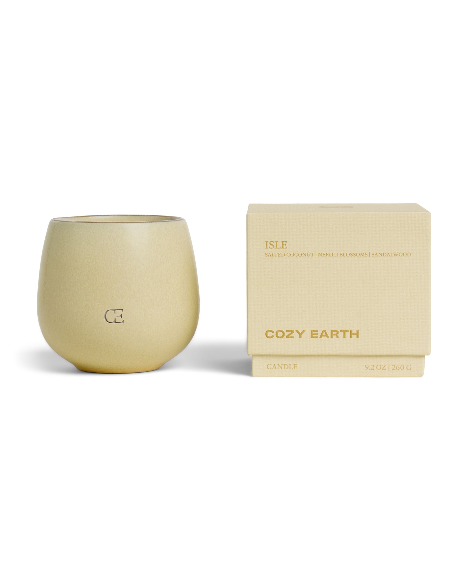 A beige Candle ISLE by Cozy Earth in a rounded holder marked "CE" sits beside its matching box, labeled with scents of salted coconut, neroli blossom, and sandalwood. Size: 9.2 oz (260 g).