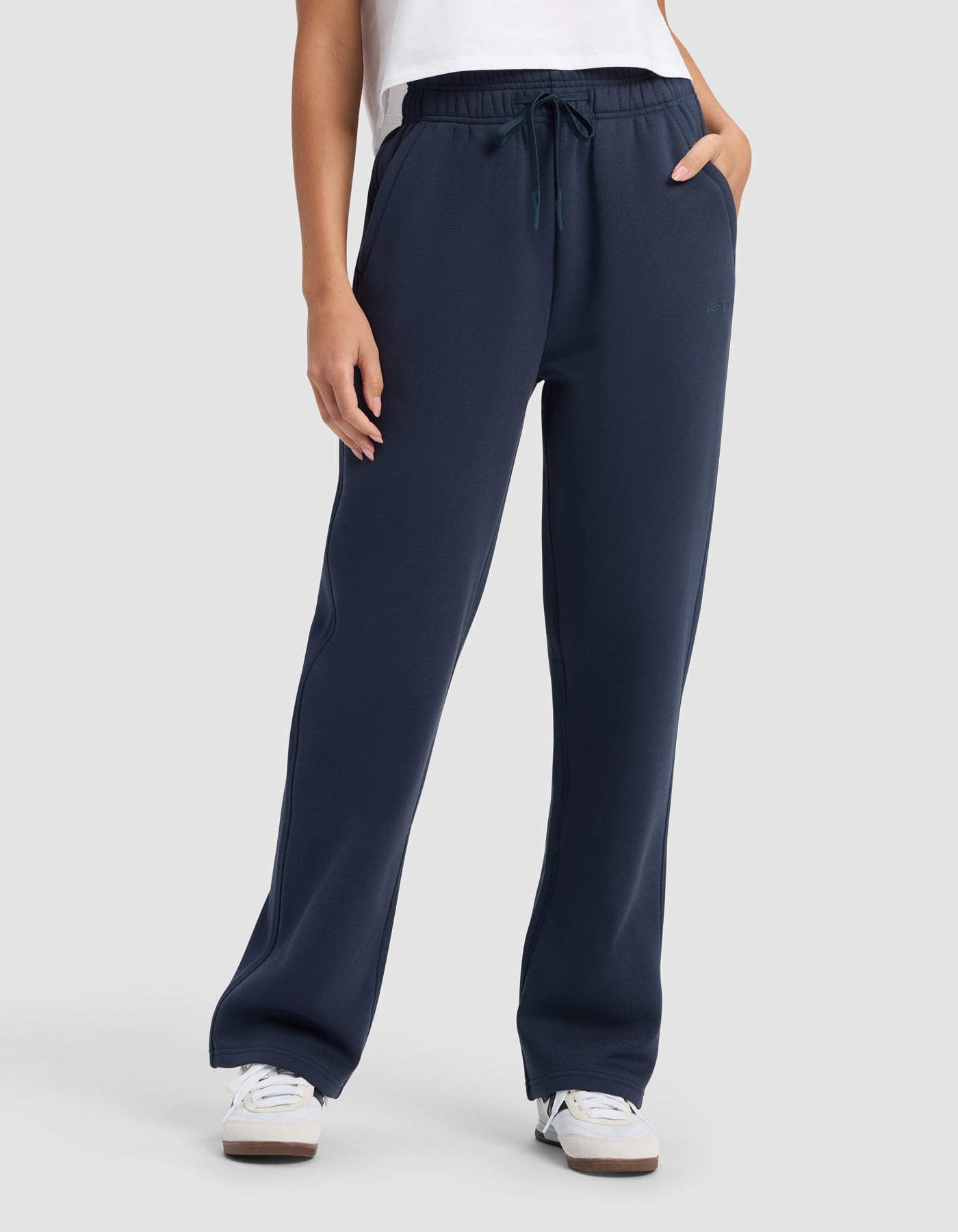 A person wearing Cozy Earth Women's Cityscape 2.0 Wide Leg Pant in navy, a white shirt, and white sneakers stands with hands in their pockets against a plain light gray background.|Color:Eclipse