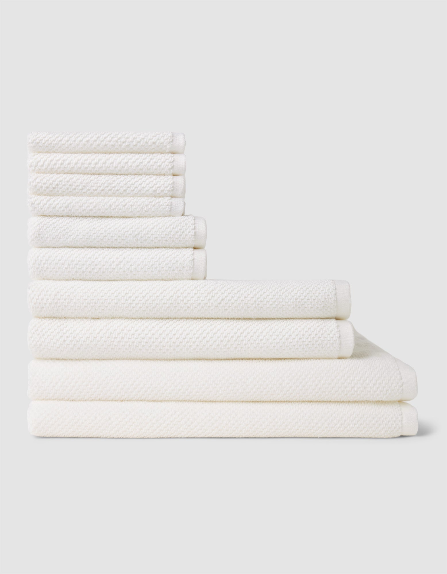 The Nantucket Bath Towel Set by Cozy Earth is shown neatly stacked by size from smallest to largest on a light gray background.