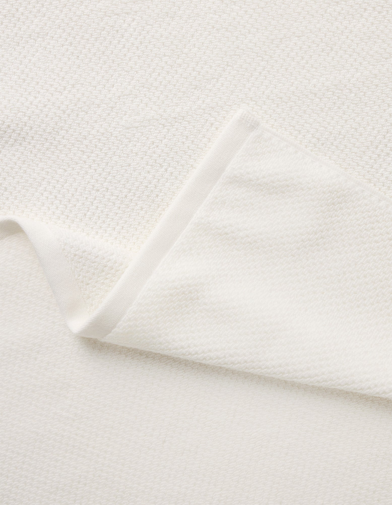 A close-up of the Cozy Earth Nantucket Bath Towel Set, featuring soft off-white textured fabric on a flat surface, highlights its plush material and clean, minimalist design.