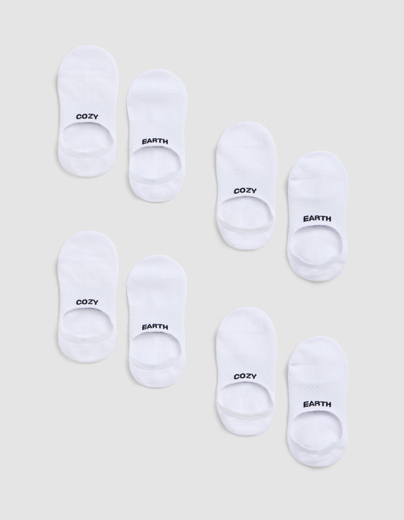 Eight pairs of white socks from the Cozy Earth Essential No-Show Sock 4-Pack are arranged on a light grey background, each sock featuring "COZY" or "EARTH" in black text at the toes.|Color:White