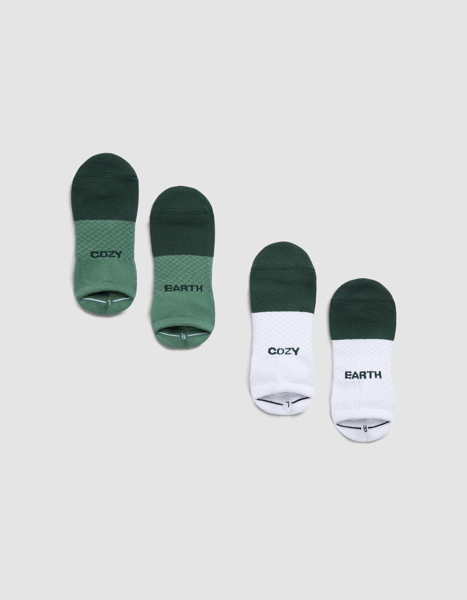 Two pairs of Cozy Earth Essential Ankle Socks on a light gray background: one green pair with "COZY" and "EARTH" text, and one white-and-green pair featuring the same words.