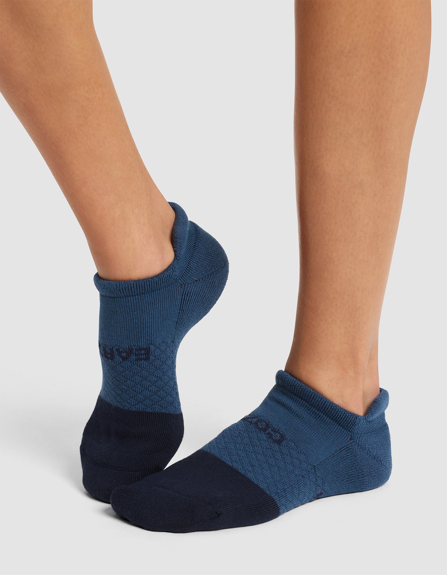 A person wears Cozy Earth's Essential Ankle Socks in blue and navy, standing with feet crossed against a light background. |Color:Eclipse