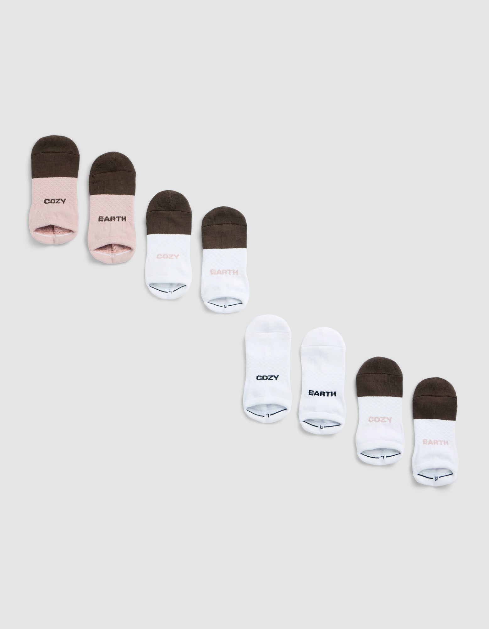 Four pairs of Cozy Earth Essential Ankle Socks in three color combos—pink with brown, all white, and brown with pink—each featuring "COZY" or "EARTH" on top, are shown diagonally on a light gray background.