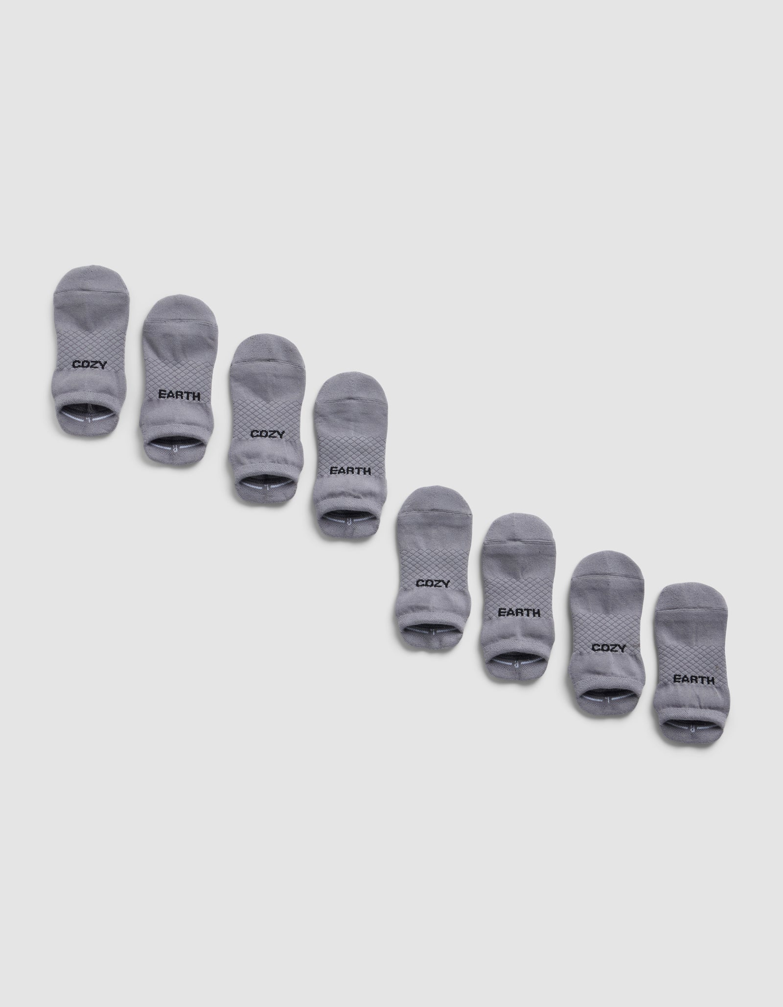 Four pairs of gray Essential Ankle Socks from Cozy Earth are arranged diagonally on a light gray background, each featuring "COZY EARTH" printed in black near the toes.