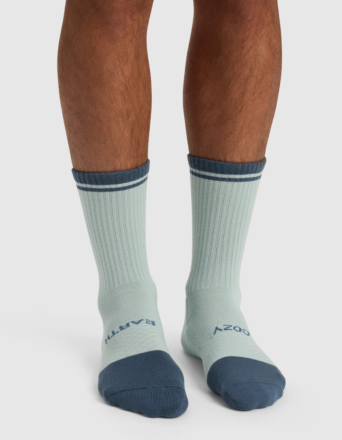 A person wearing Cozy Earth’s Essential Calf Sock – Last Chance in light blue with dark blue toes, heels, and cuffs. "EARTH" is written on the left sock top and "COZY" on the right.|Color:Arctic