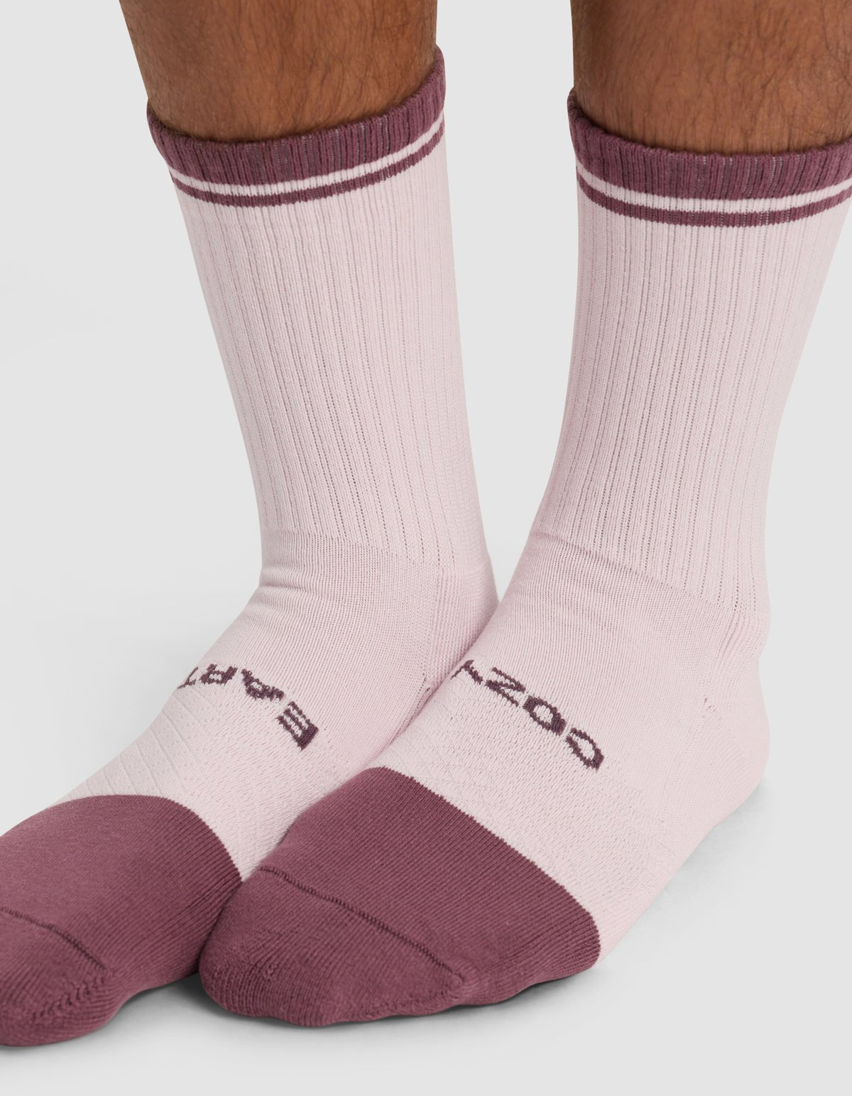 A close-up shows feet in Cozy Earth's Essential Calf Sock - Last Chance, featuring light pink with dark pink toes, heels, and stripes. "BARE" is on one sock and "DOZEN" on the other, set against a white background.
