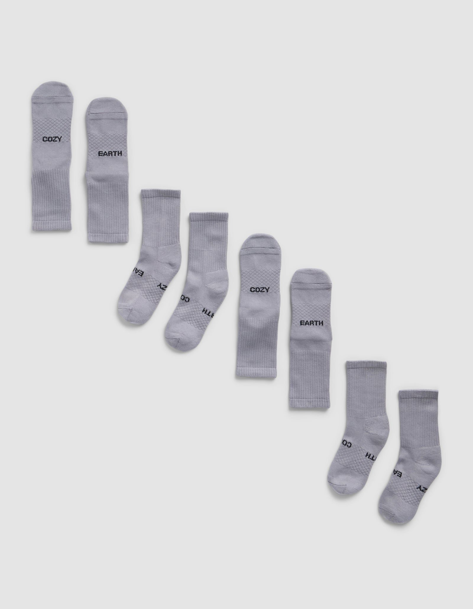 Eight pairs of Cozy Earth Essential Calf Socks, shown side by side in light gray on a white background, display both top and bottom views. Some socks feature black text near the cuffs and toes.