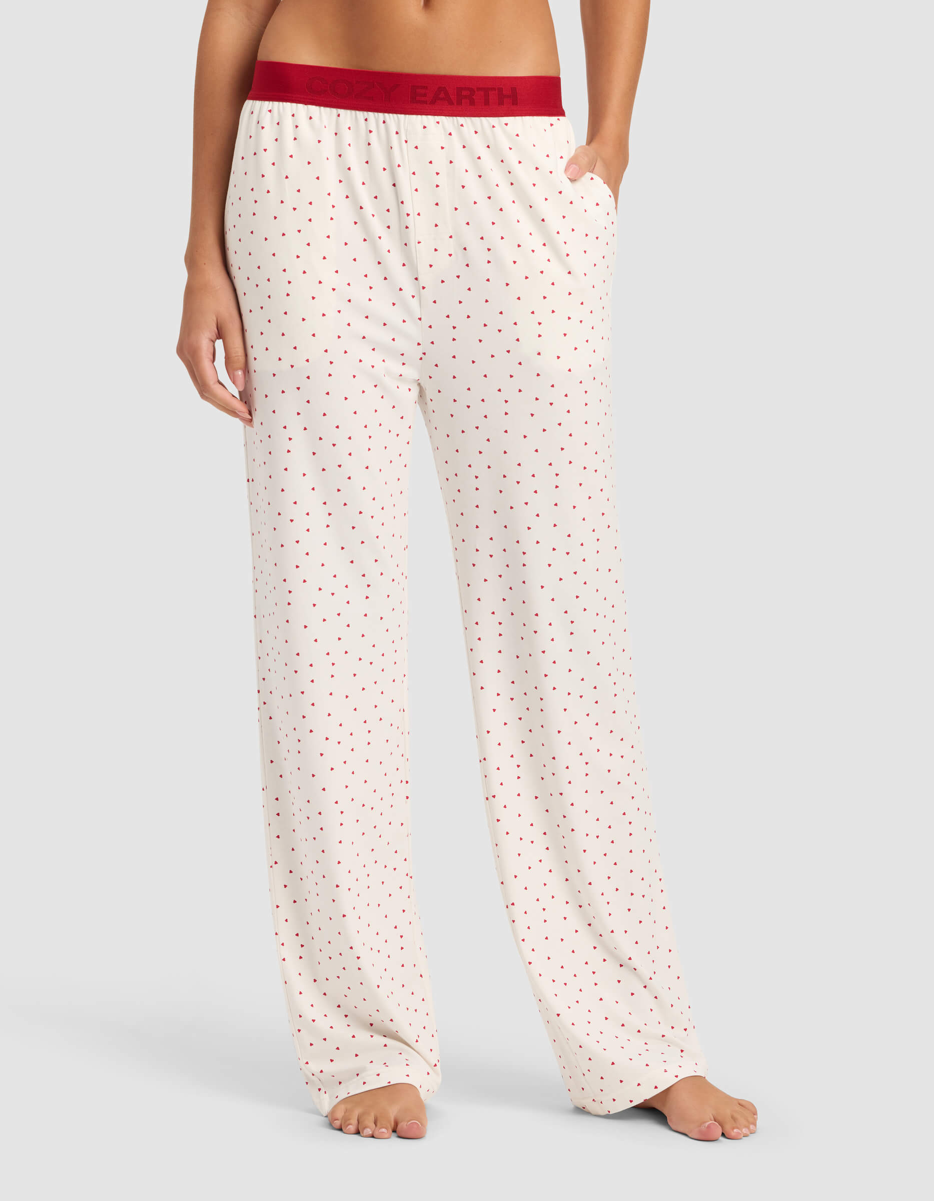 A woman models Cozy Earth's Women's First Layer Pajama Pant in cream with small red polka dots and a red waistband, standing barefoot against a plain background.|Color:Cranberry Sea Salt Mini Heart