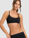 A woman with long brown hair wears the Women's First Layer Pajama Soft Bra & Pant Set by Cozy Earth in black, standing confidently against a plain light background with one arm bent.|Color:Jet Black