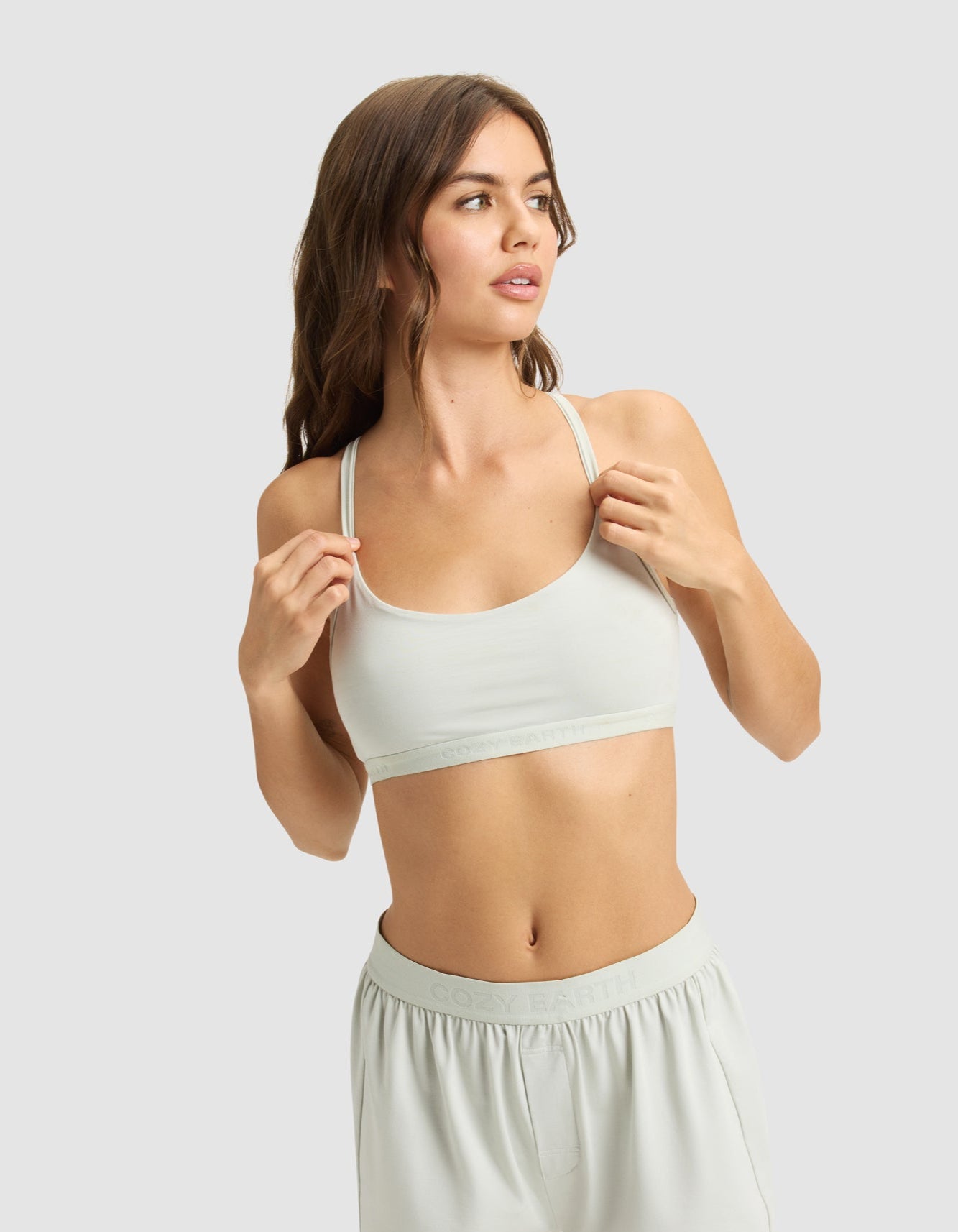 A woman with long brown hair models the Cozy Earth Women's First Layer PJ Soft Bra and matching shorts, standing against a plain light gray background and looking to the side.|Color:Laurel