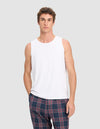 A man wears the Cozy Earth Men's First Layer Pajama Tank in white, paired with blue plaid pants, standing against a light gray background and looking directly at the camera with a neutral expression.|Color:White
