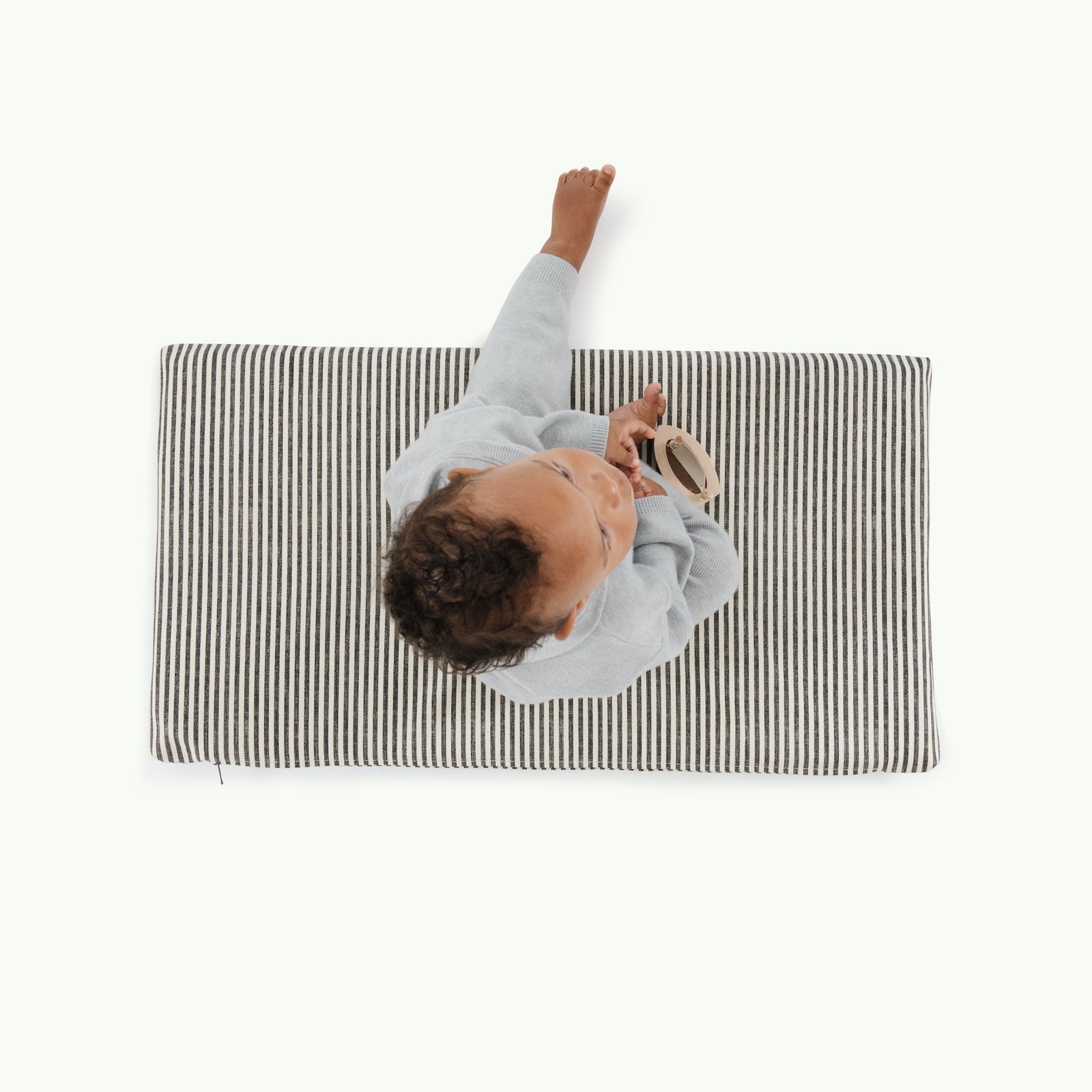 A child sits on a Gathre Wholesale Padded Changing Mat, dressed in gray and holding a circular item, viewed from above against a plain white background.