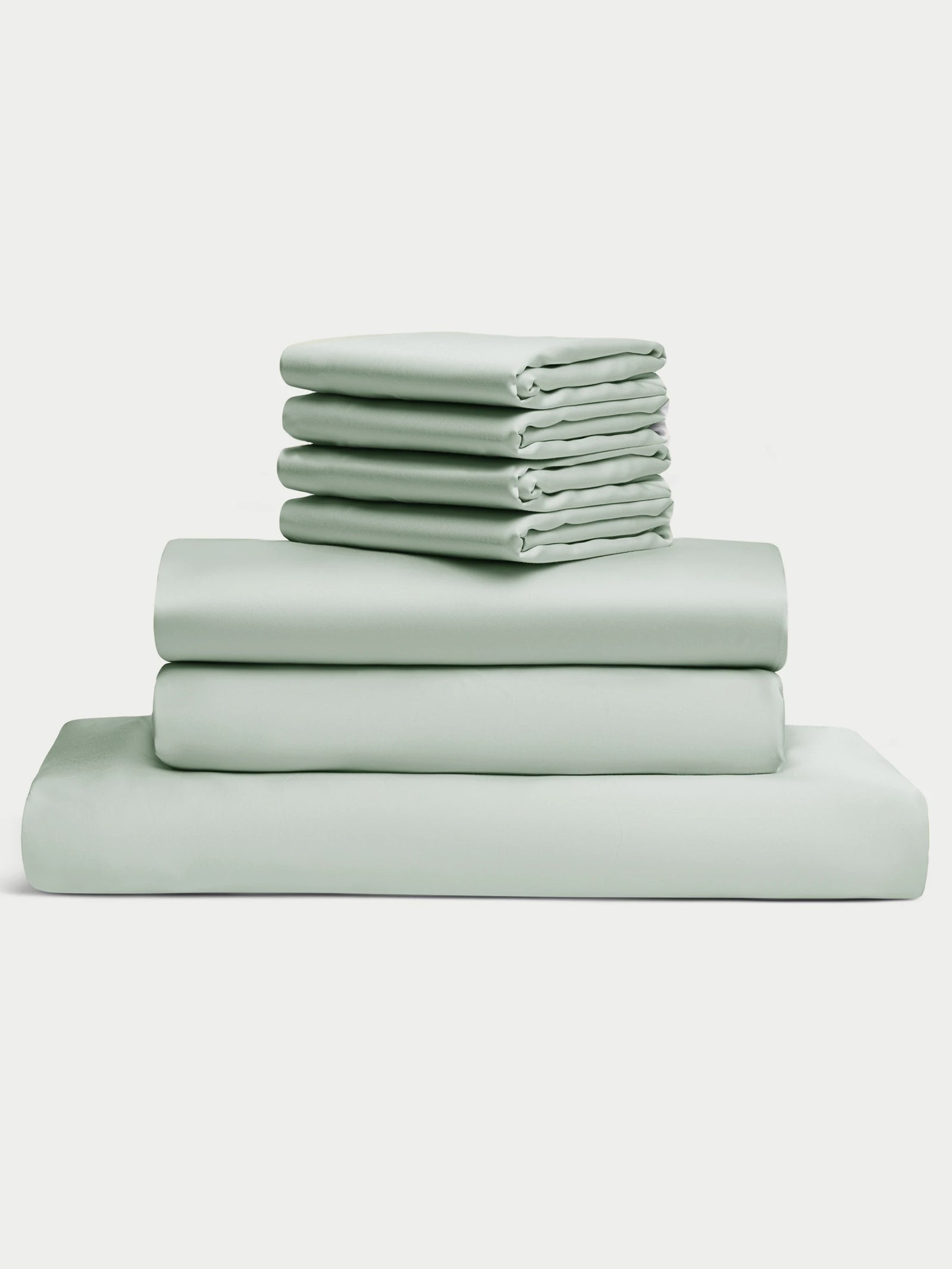 A neatly stacked Bamboo Bedding Core Bundle by Cozy Earth, featuring light green flat and fitted sheets along with pillowcases, arranged on a plain white background.