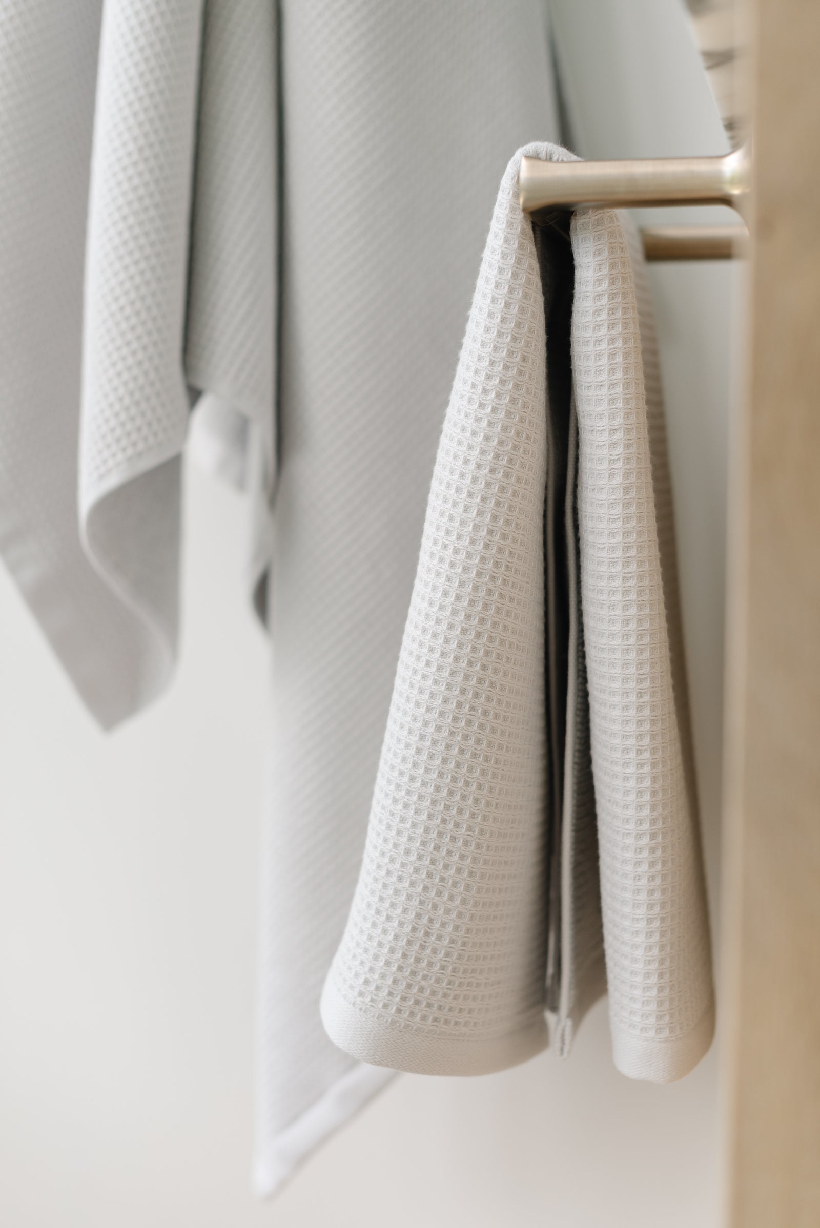 Waffle Hand Towel in the color Light Grey. Photo of Light Grey Waffle Hand Towel taken with the Light Grey Waffle Hand Towel hung from a towel ring. The picture was taken in a bathroom.
