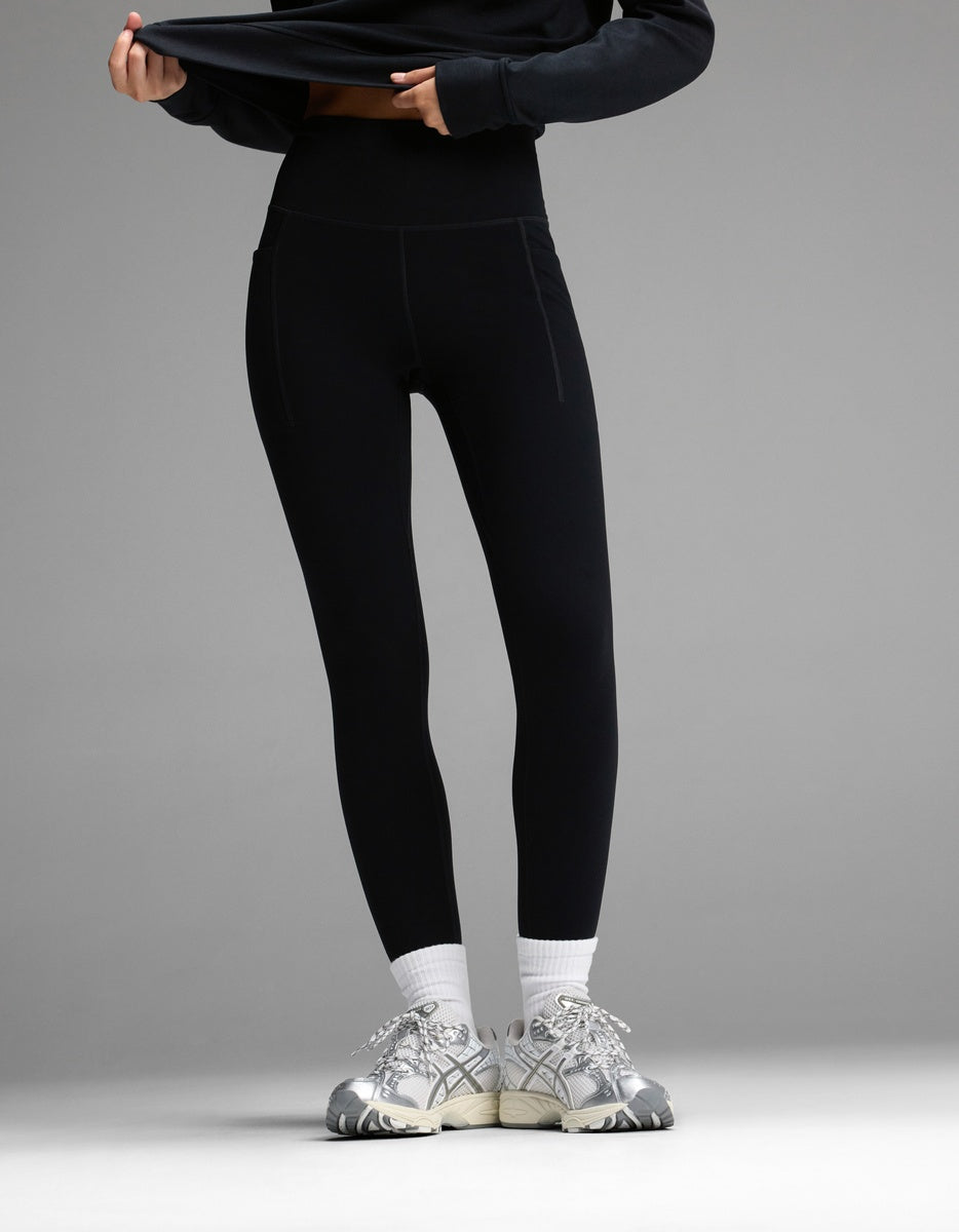 A person wearing black Women’s Liv Leggings with Pockets, white socks, and silver running shoes.|Color:Jet Black