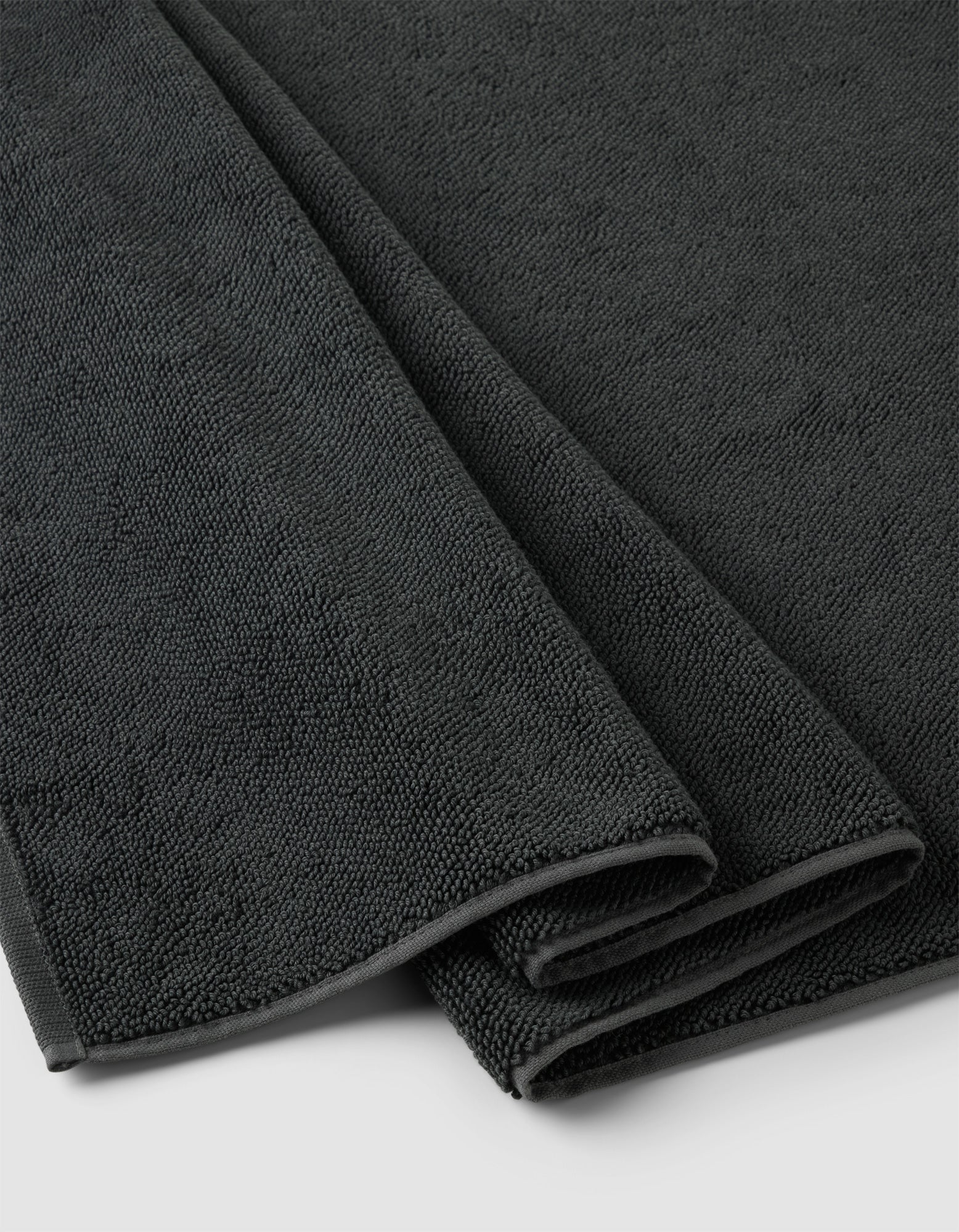 A close-up of the Cozy Earth Loop Terry Bath Mat, neatly folded in dark gray with a soft, textured surface, displayed on a light-colored background.