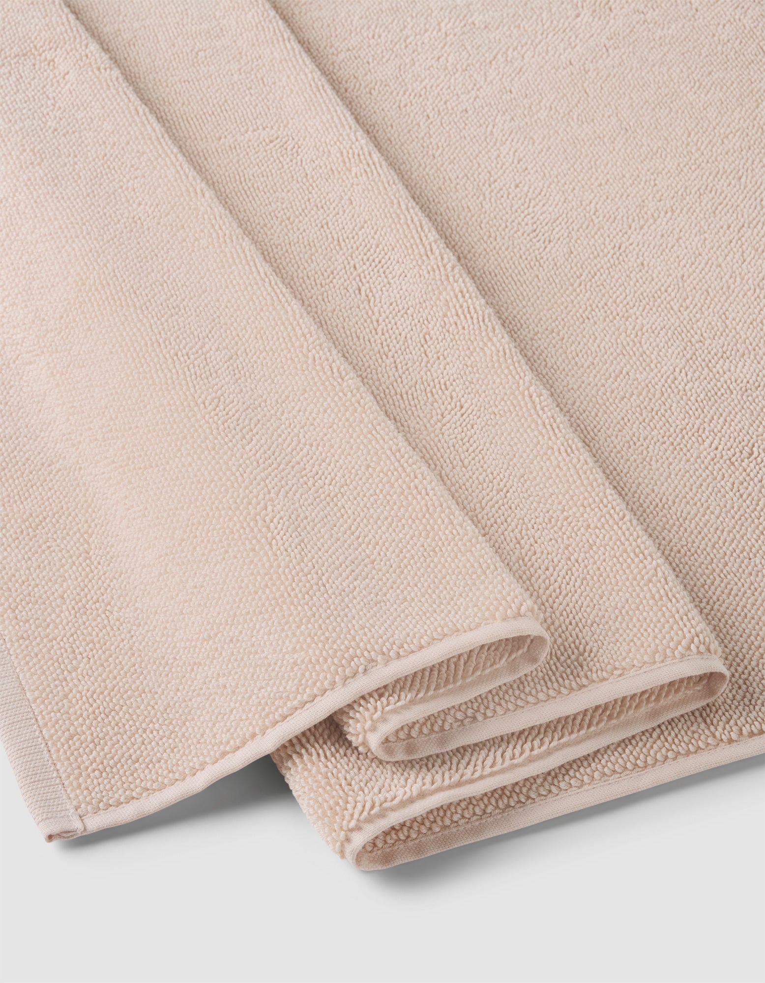 A Loop Terry Bath Mat by Cozy Earth, in light beige with a soft, textured surface, is neatly folded and stacked on a white background.