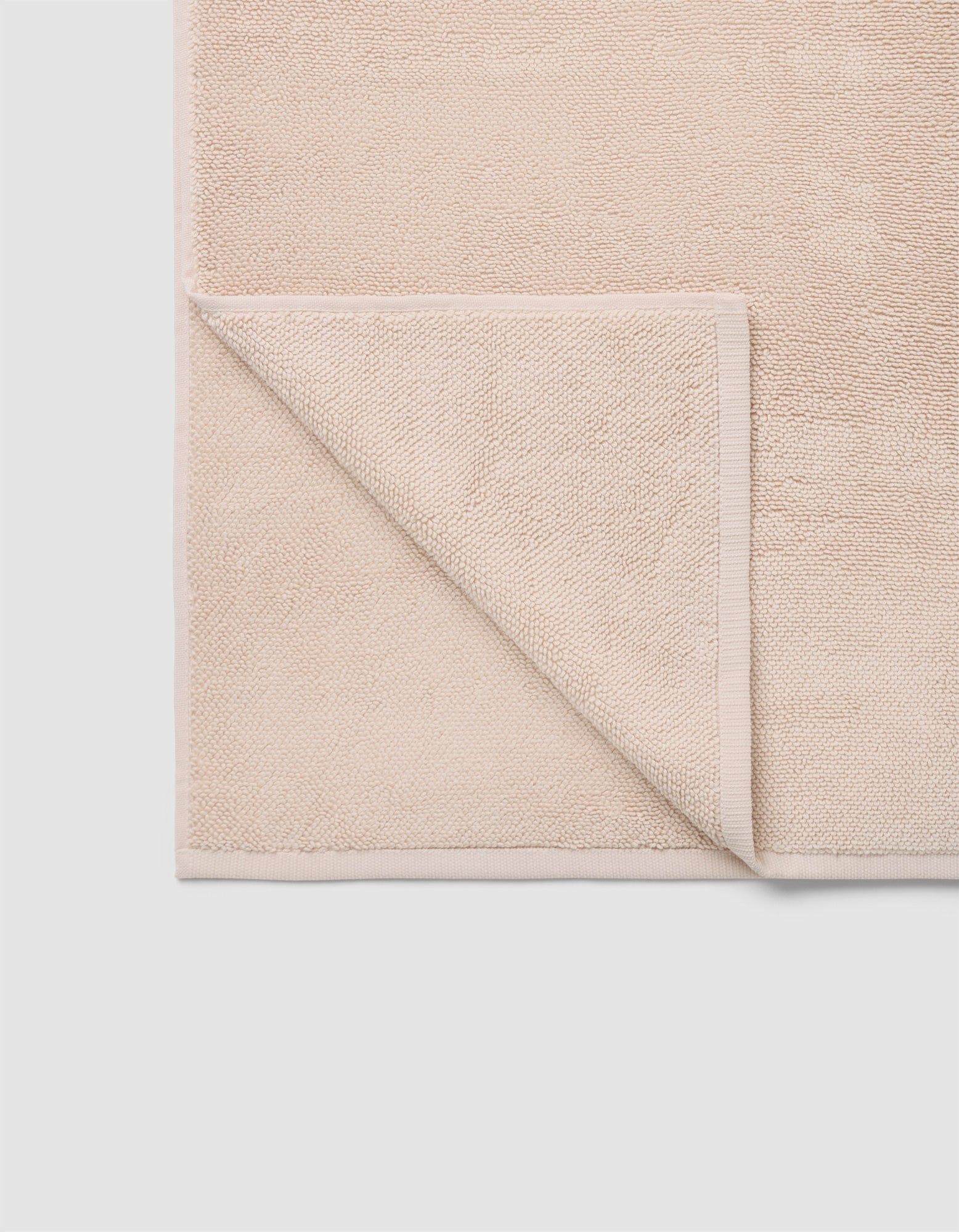 The Cozy Earth Loop Terry Bath Mat is a beige, rectangular mat with one corner folded to reveal its textured underside. Its simple design rests on a light-colored surface.