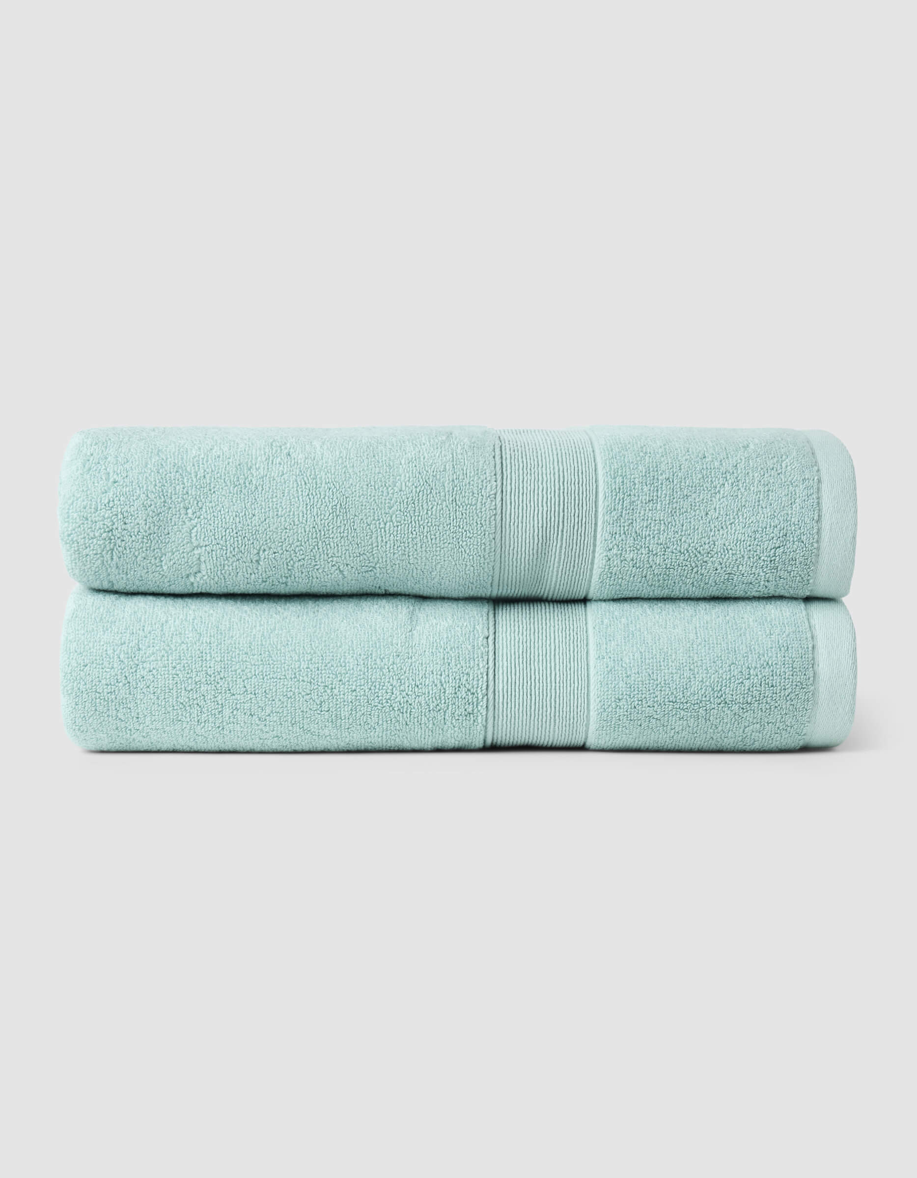 Two Luxe Bath Towels by Cozy Earth, neatly folded and stacked, are displayed against a plain light gray background.|Color:Tide