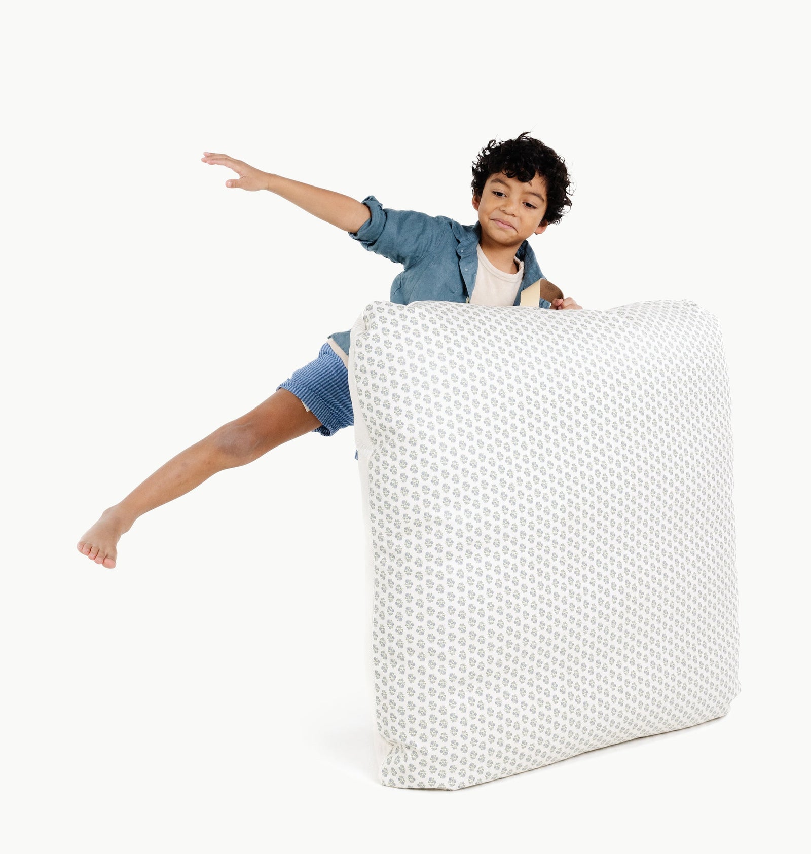 A young child excitedly jumps onto the Gathre Wholesale Floor Cushion in Meadow, playfully stretching out an arm against a white background.
