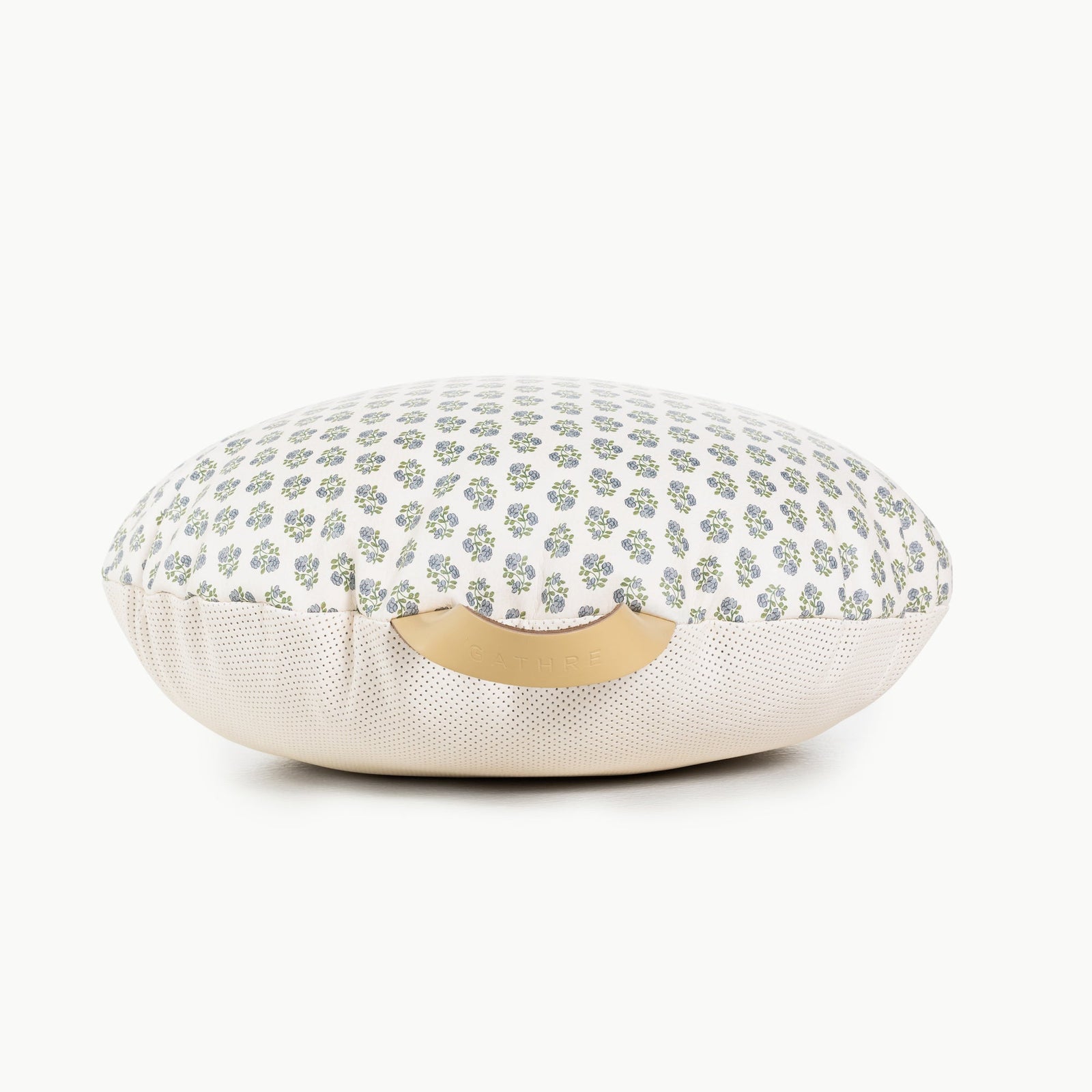 The Gathre Wholesale Floor Cushion features a round, cushion-like shape with a white and light green floral top, beige mesh sides, and a beige handle on the front.