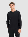 A young man with short, curly brown hair models the Cozy Earth Men's Bamboo Stretch-Knit Long Sleeve in black, paired with matching pants. He stands against a light gray background with a neutral expression and one hand in his pocket. |Color:Black