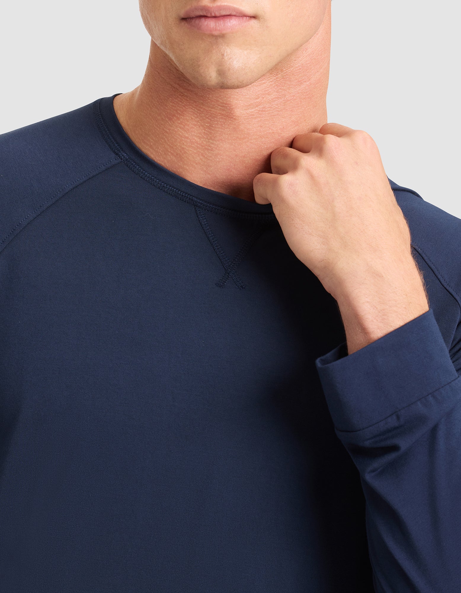 A man wears the Cozy Earth Men's Bamboo Stretch-Knit Long Sleeve in navy blue, with his fist near his collarbone. Only his lower face and upper torso are visible against a light gray background.