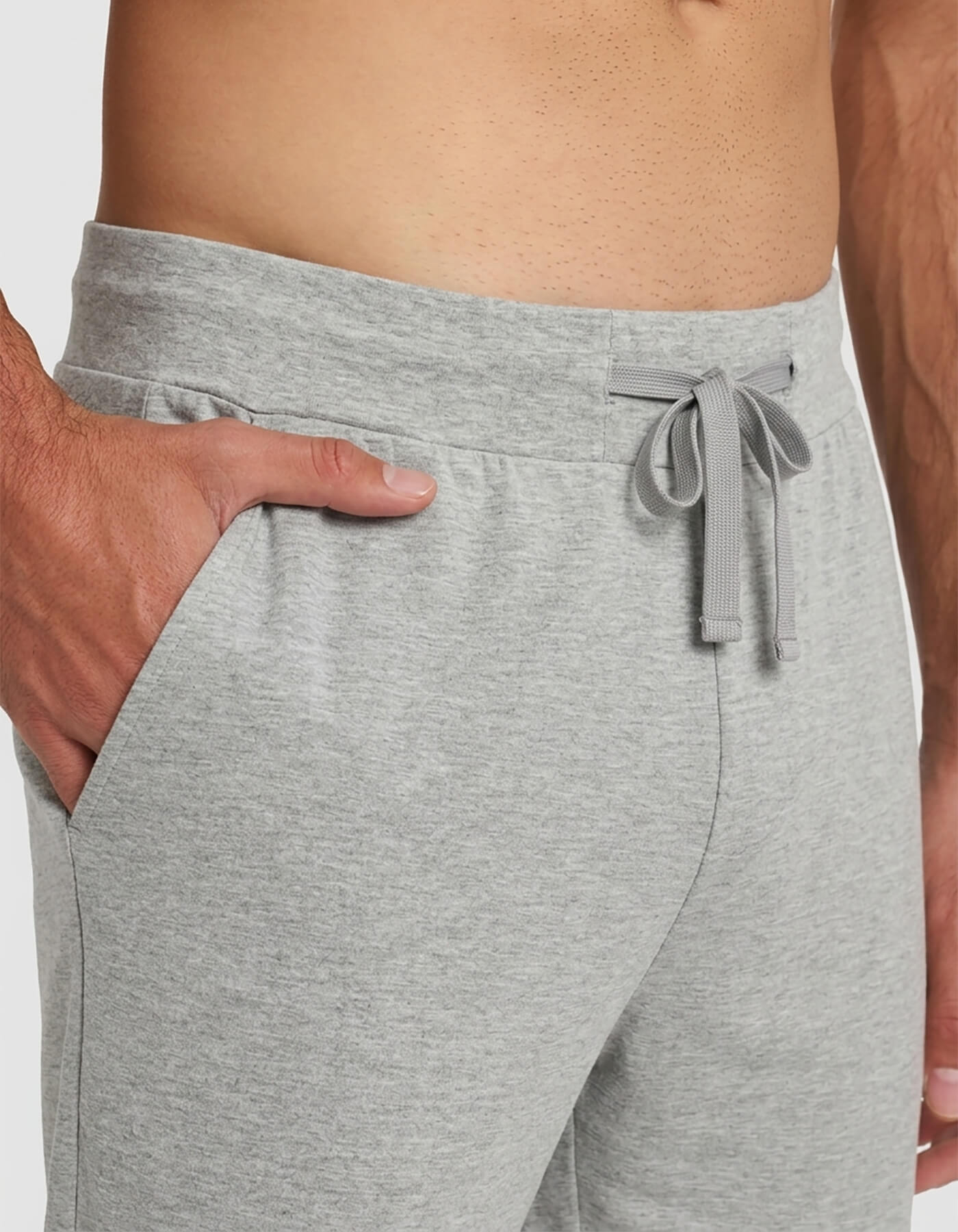 A close-up of a person wearing Cozy Earth's Men's Bamboo Stretch-Knit Short Sleeve Pajama Set, featuring light gray drawstring waist pants with one hand in the pocket and a bare torso visible.|Color:Heather Grey