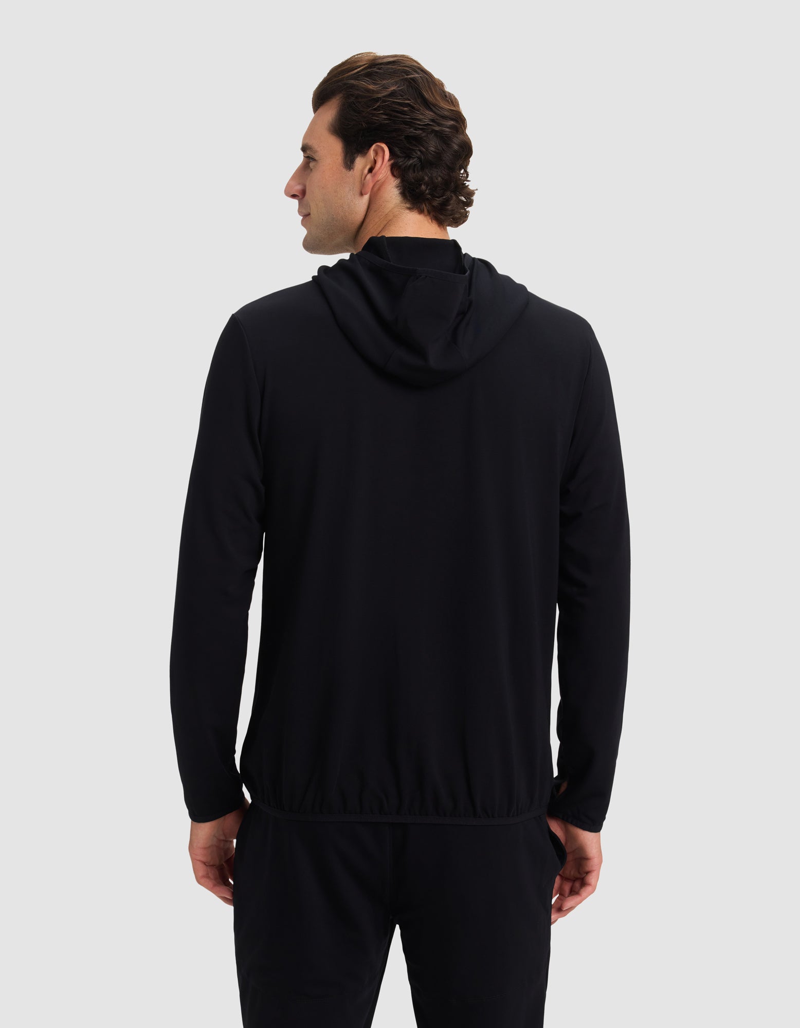 A man faces away from the camera, wearing Cozy Earth's Men's Brushed Bamboo Recovery Hoodie in black with matching pants, set against a plain light gray background.