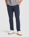 A person stands with hands in pockets against a plain background, wearing Cozy Earth's Men's Everywhere Pant in navy blue, a gray shirt, and white sneakers with light brown soles.  |Color:Eclipse