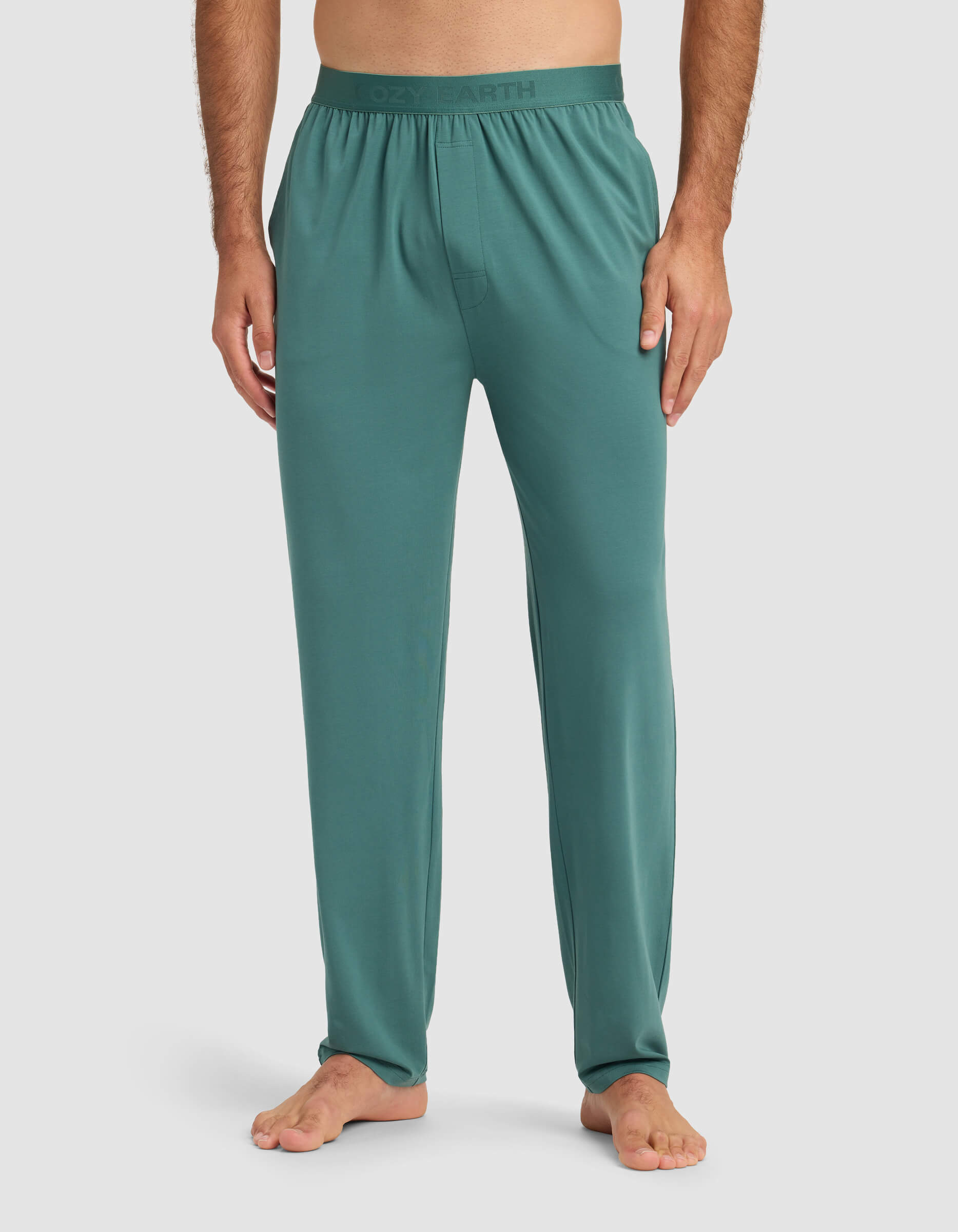 A man stands barefoot wearing Cozy Earth's Men's First Layer Pajama Pant in teal with an elastic waistband and no visible pockets, shown from the waist down against a plain light background.|Color:Sea Green