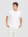 A young man models the Cozy Earth Men's First Layer Pajama Short Sleeve Tee and light plaid pajama pants against a light gray background, looking to his left while holding the hem of his shirt.|Color:White