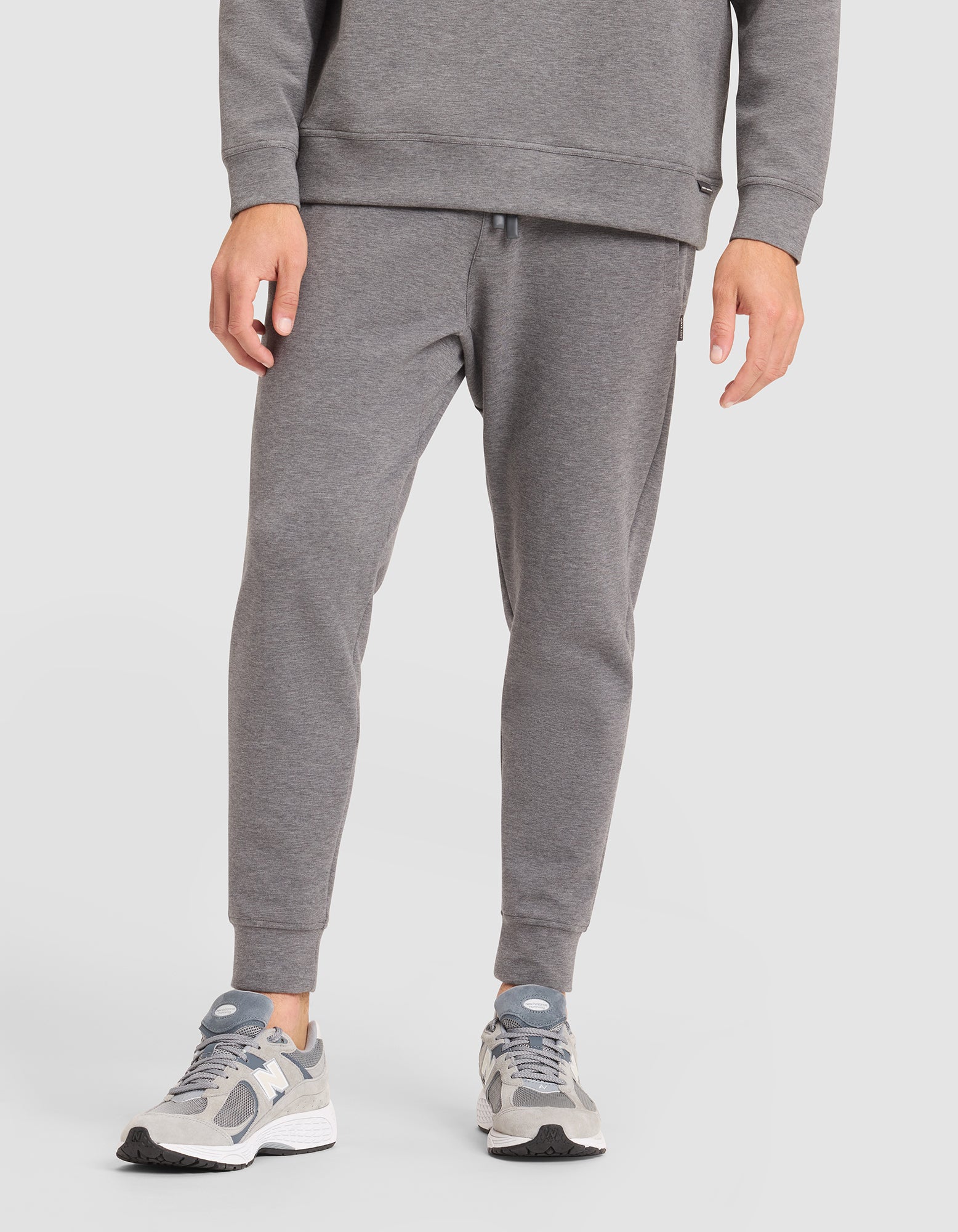 A person is shown from the waist down, wearing Cozy Earth's Men's StretchTech Jogger in gray with a matching sweatshirt and gray-white sneakers, standing against a plain white background. |Color:Coal Heather