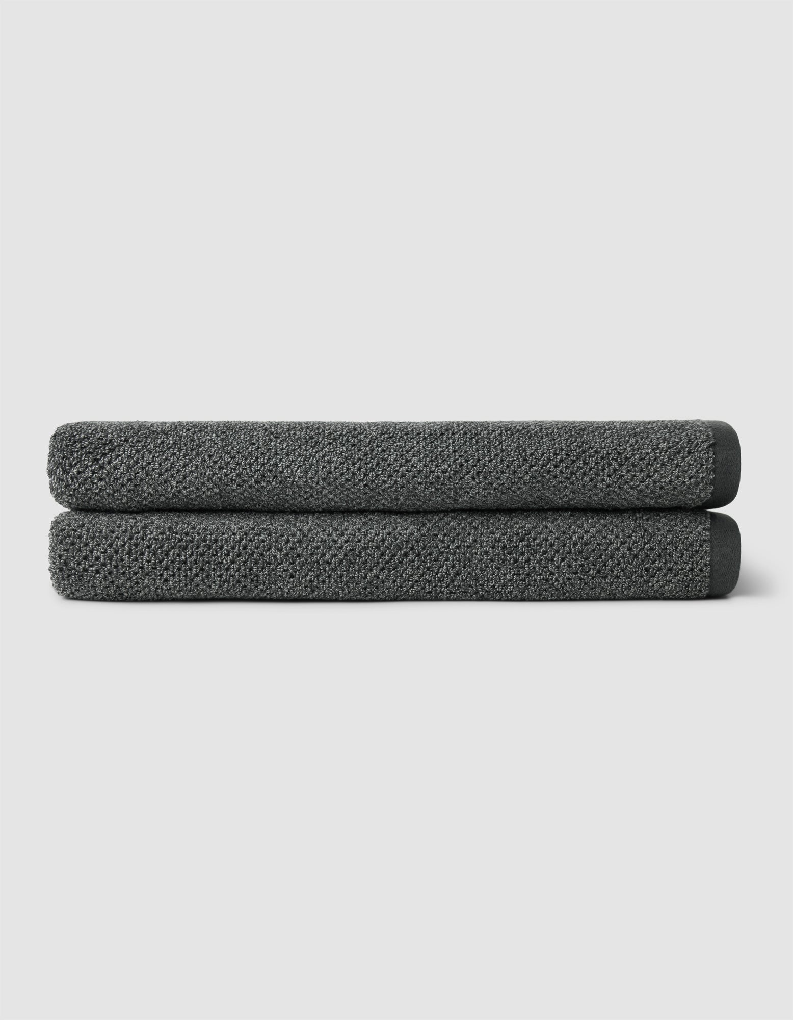 Two neatly folded Cozy Earth Nantucket Bath Sheets in dark gray are stacked on top of each other against a plain light gray background.|Color:Graphite